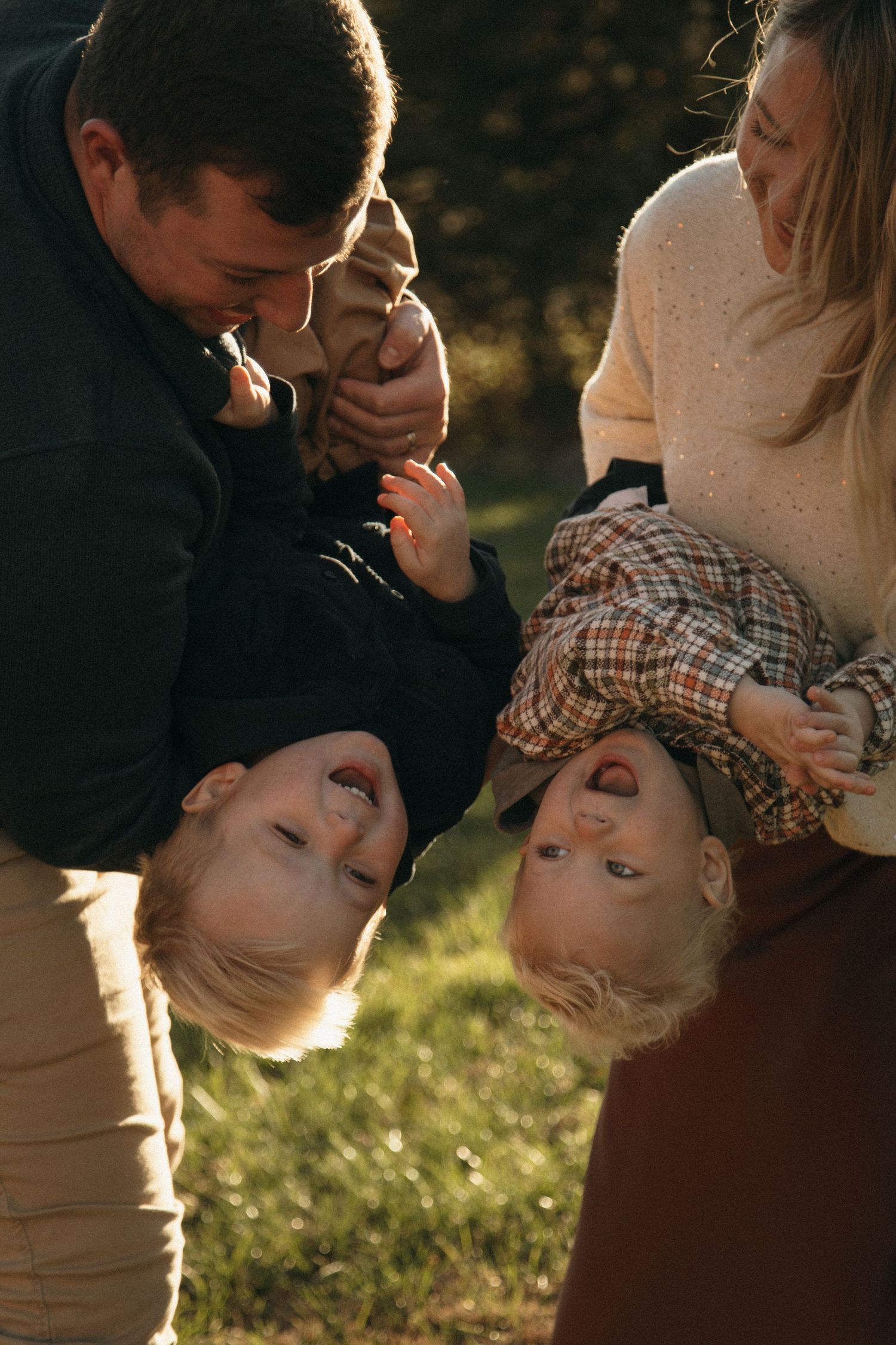 Playful family moment captured during sunset with children being held upside down.