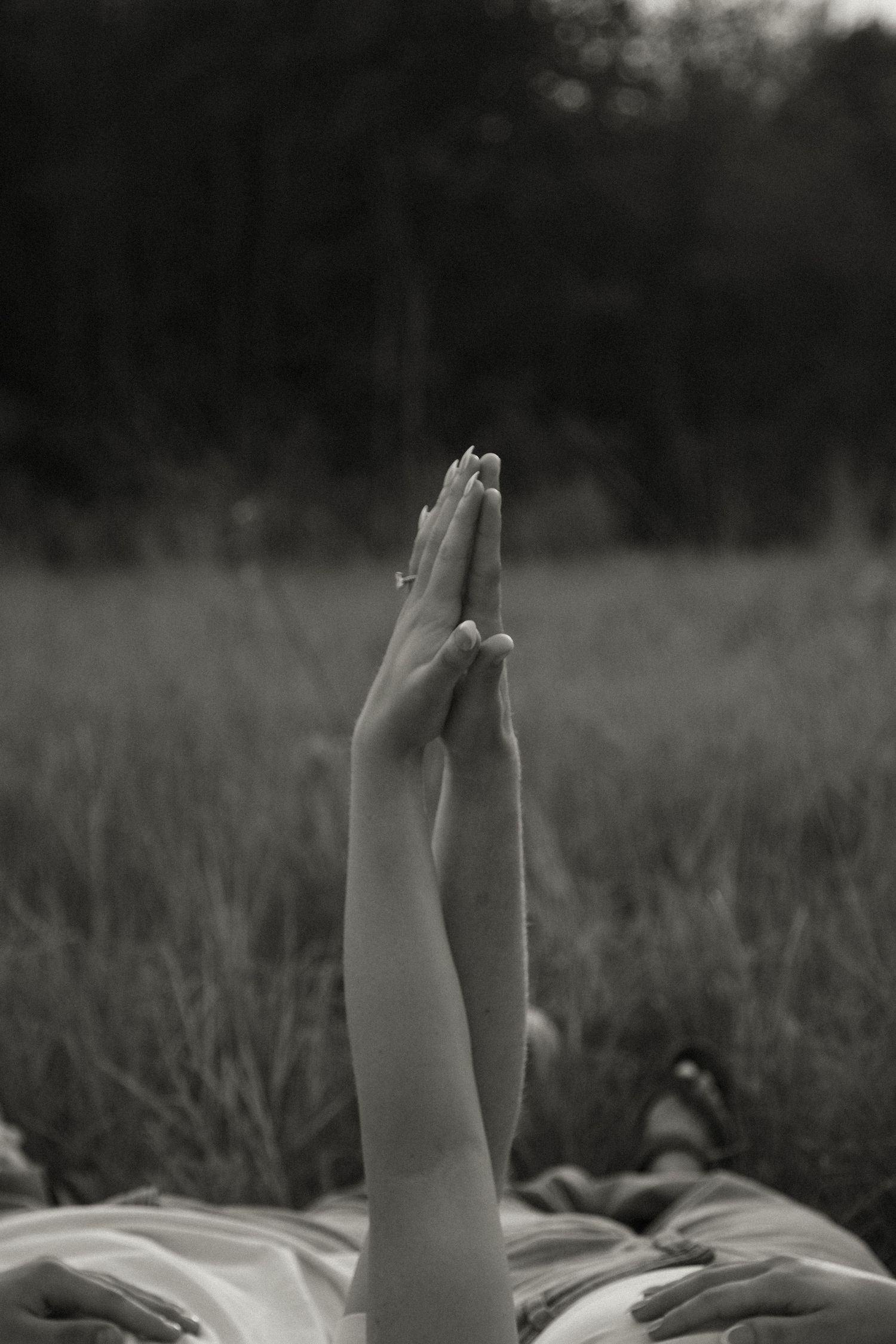 Black and white photo of two hands pressed together in prayer pose above a grassy field.