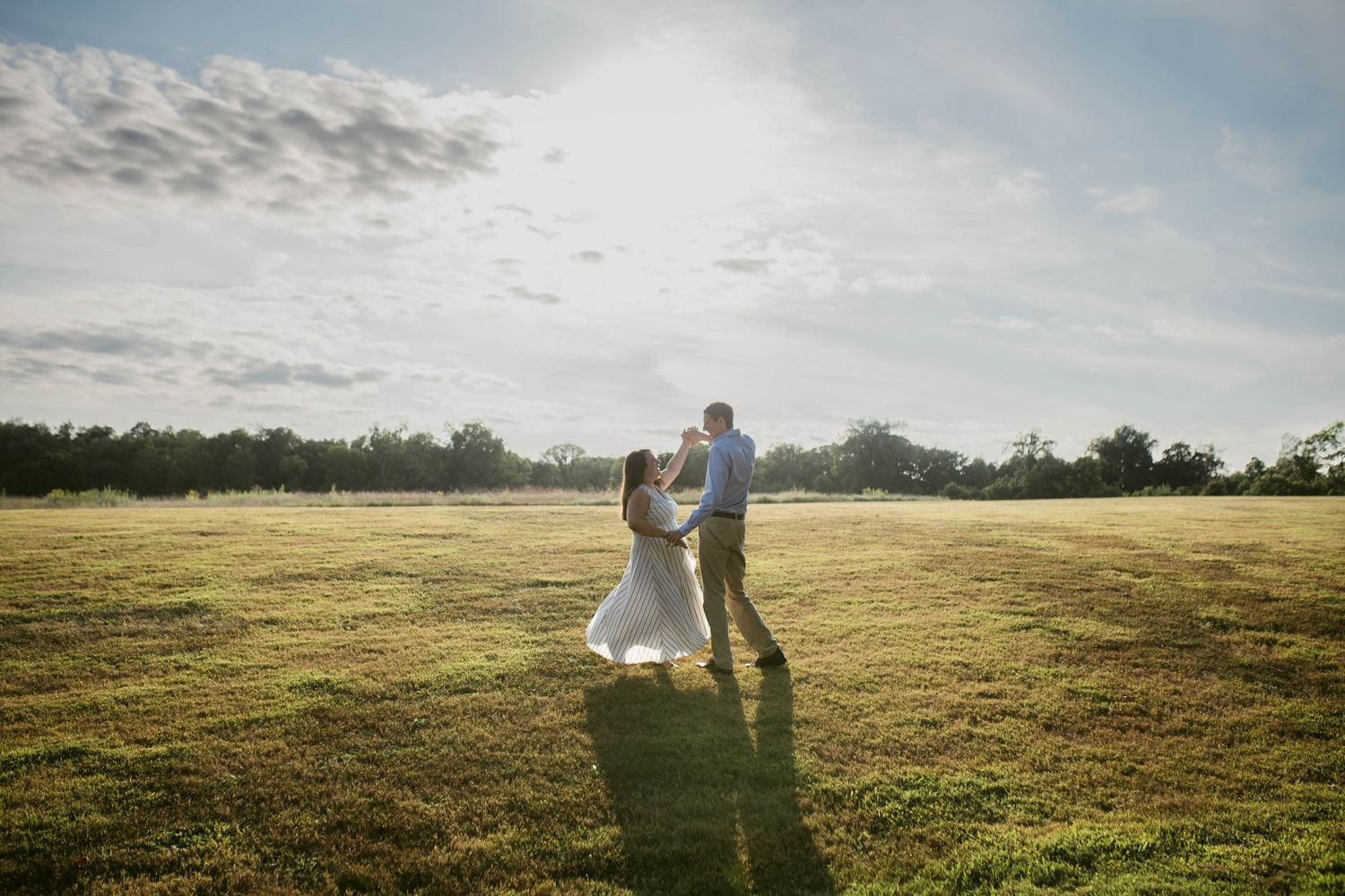 Couple dancing in sunlit open field on wedding day, wearing white dress and khakis, with trees and blue sky backdrop.
central Illinois