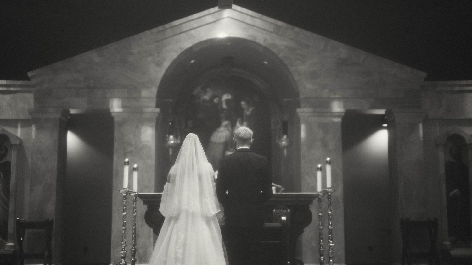 Black and white photo of a bride and groom standing at a candlelit church altar during their wedding ceremony. central Illinois