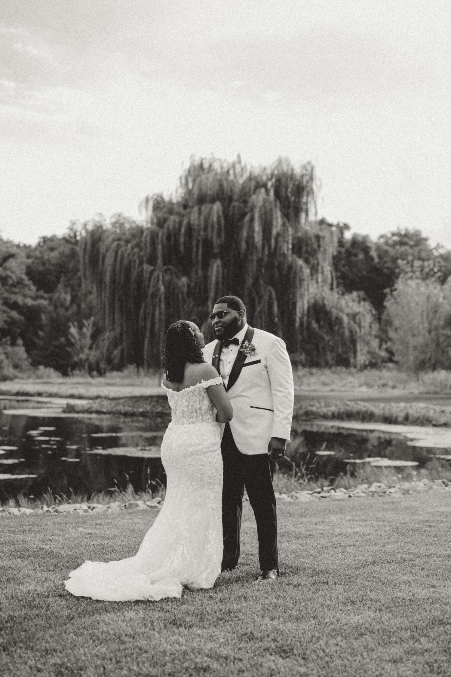 Black and white photo of a bride and groom standing by a pond with a weeping willow tree backdrop. central Illinois