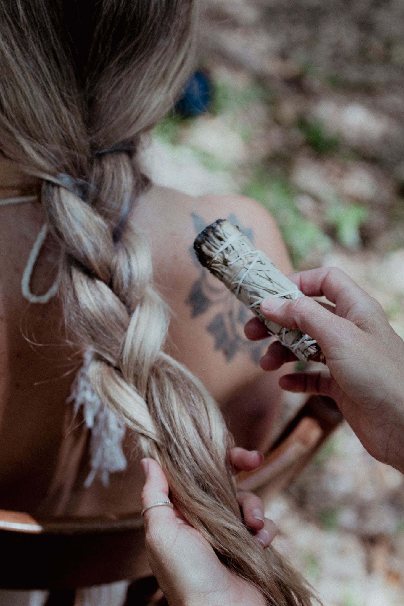 Hands holding a bundle of sage near a braided hairstyle with visible tattoo.