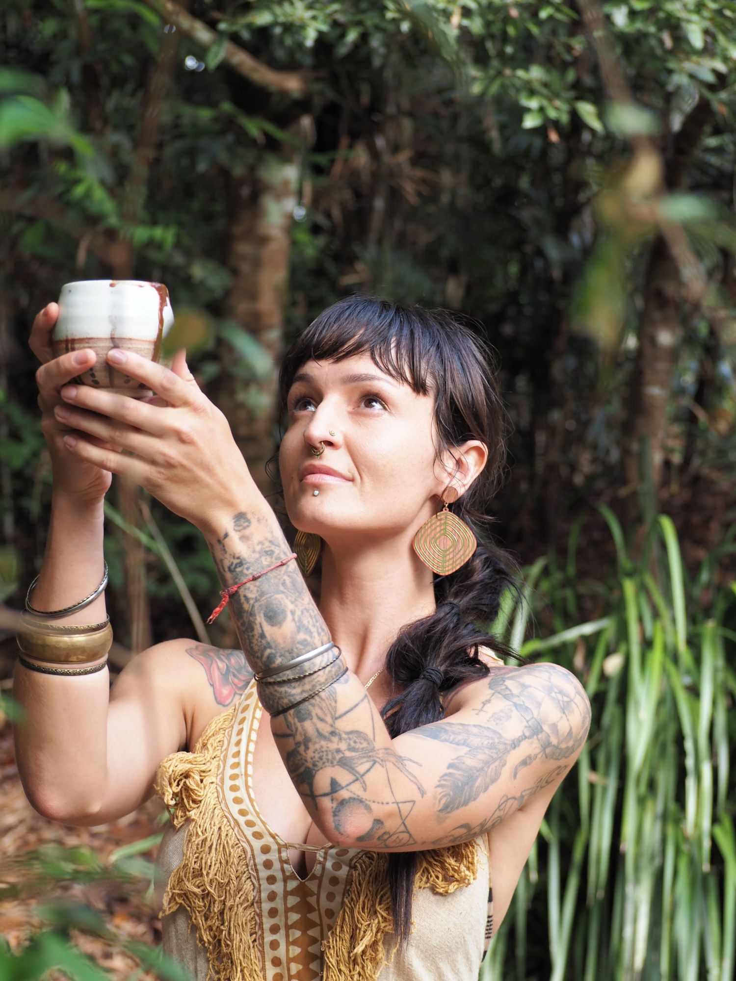 A tattooed person in a gold and white dress poses artistically in a garden setting.