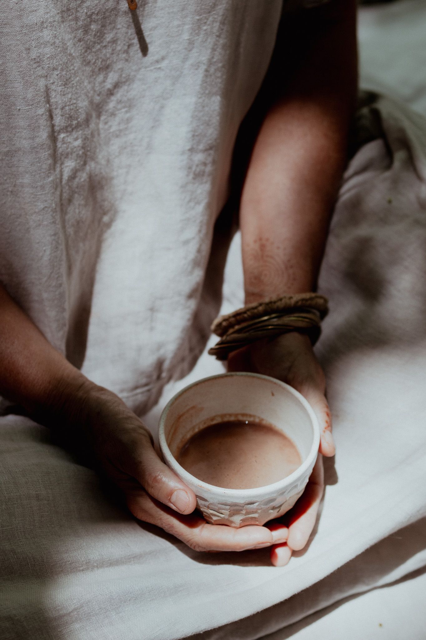 Hands holding a white ceramic bowl in soft, moody lighting.