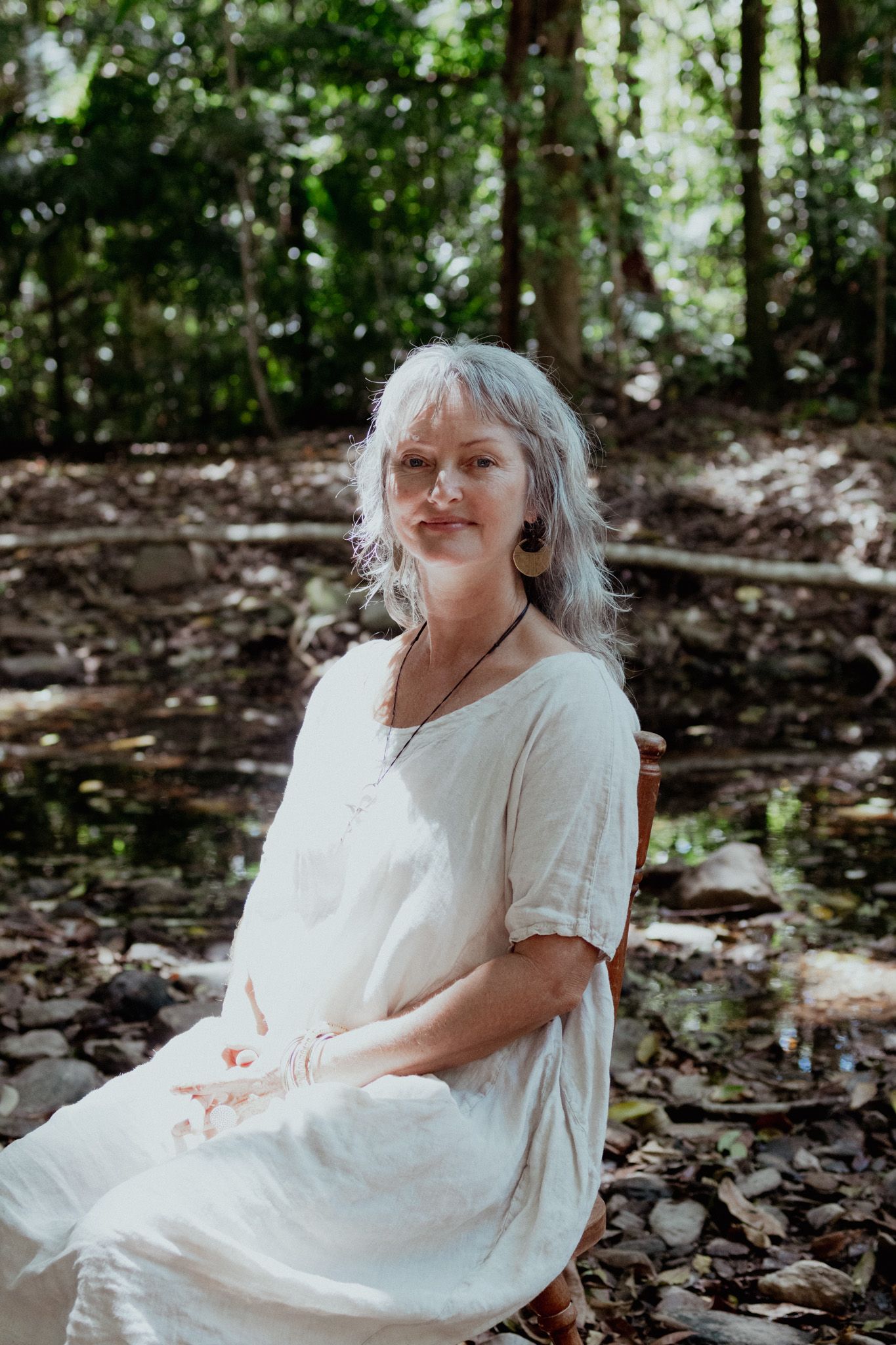 A peaceful outdoor portrait showing someone in white clothing seated in a wooded setting.