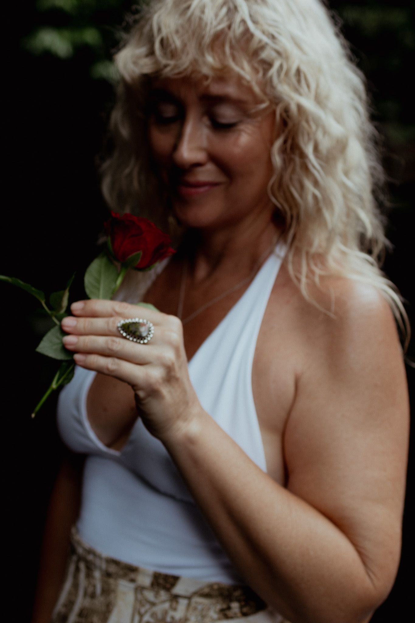 Person in white top holding and examining a small red flower in natural lighting.