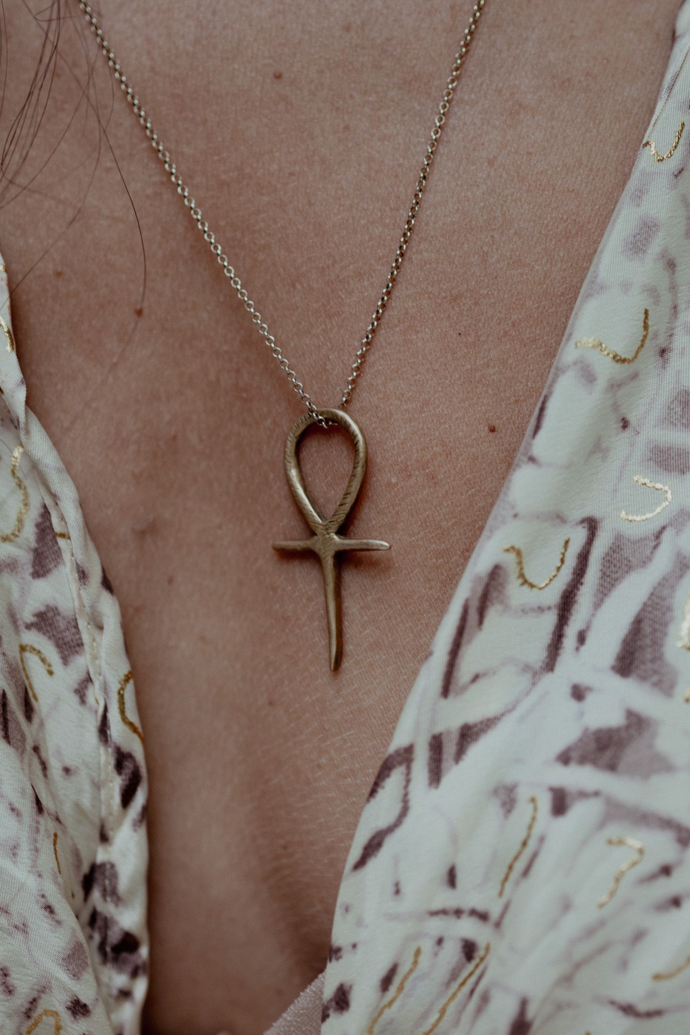 A delicate gold cross pendant necklace displayed against a textured brown background.