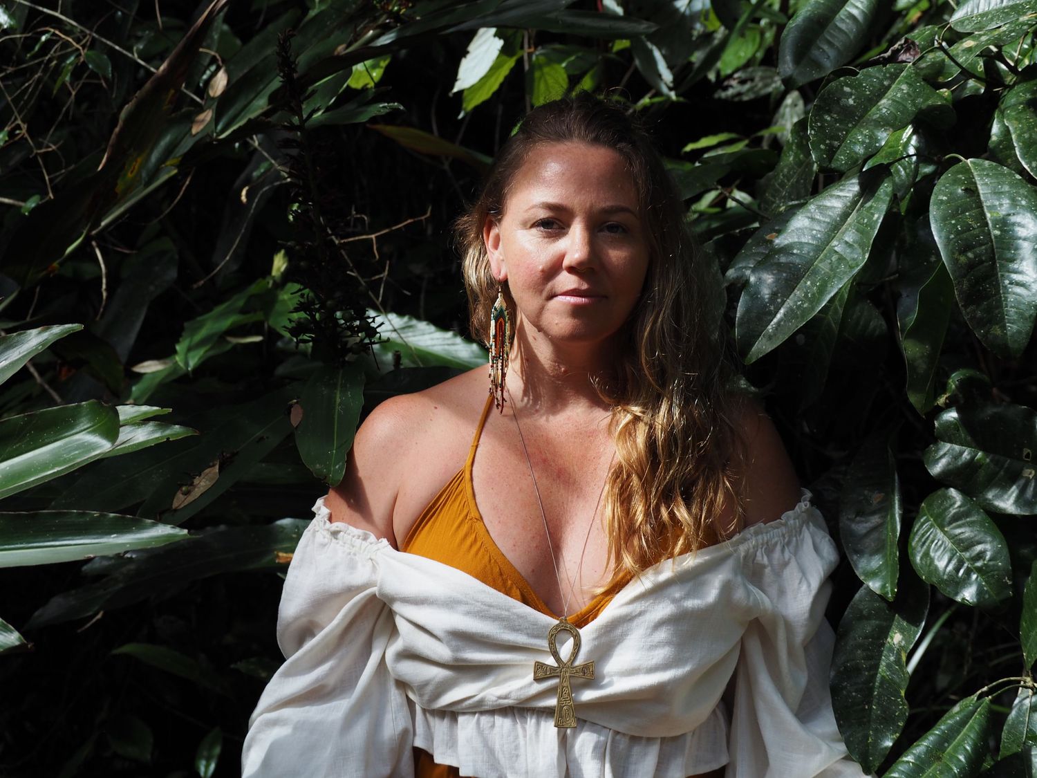 Woman in yellow top and white shirt poses against tropical foliage background.
