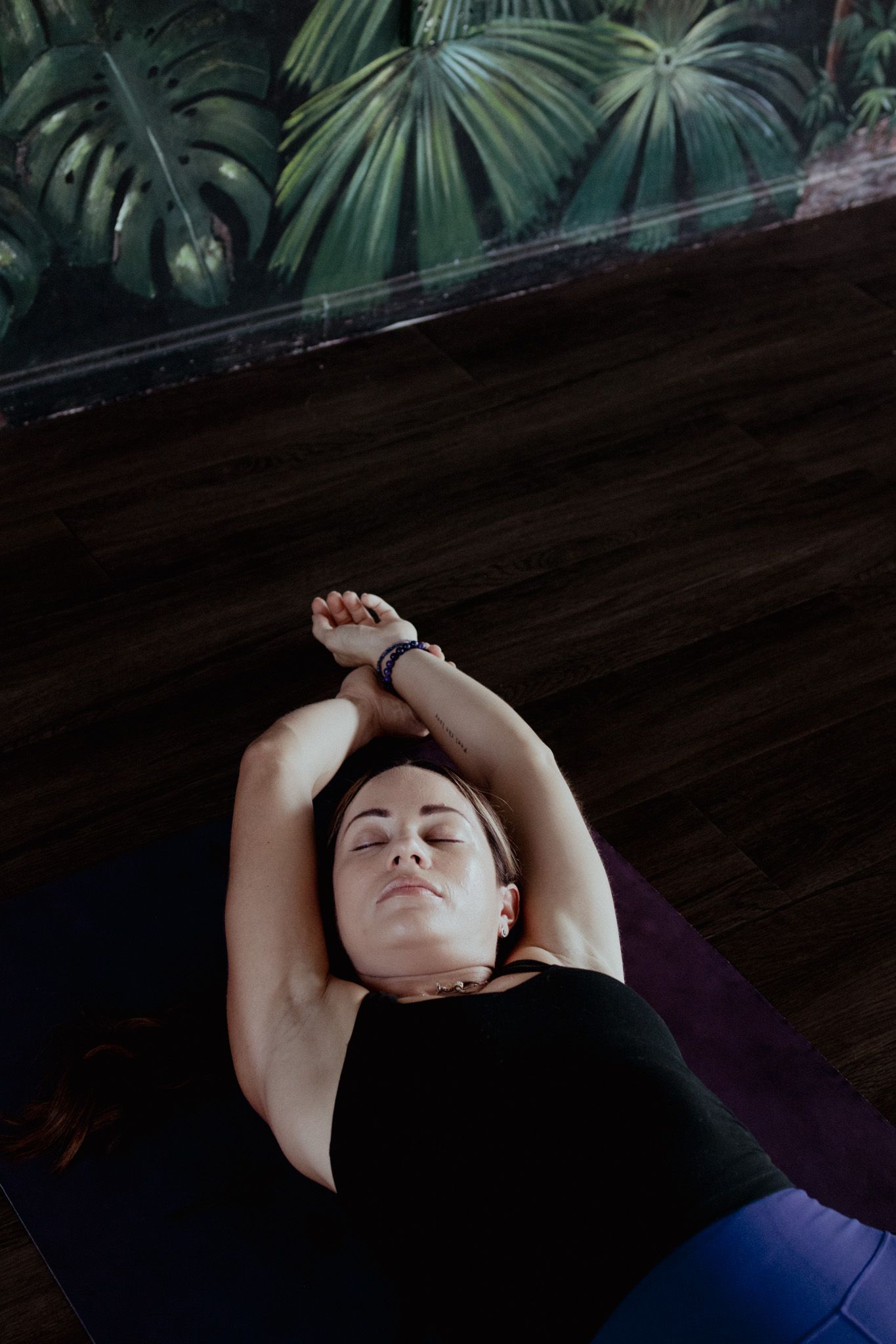 Person lying in relaxation pose on yoga mat against tropical wallpaper background.