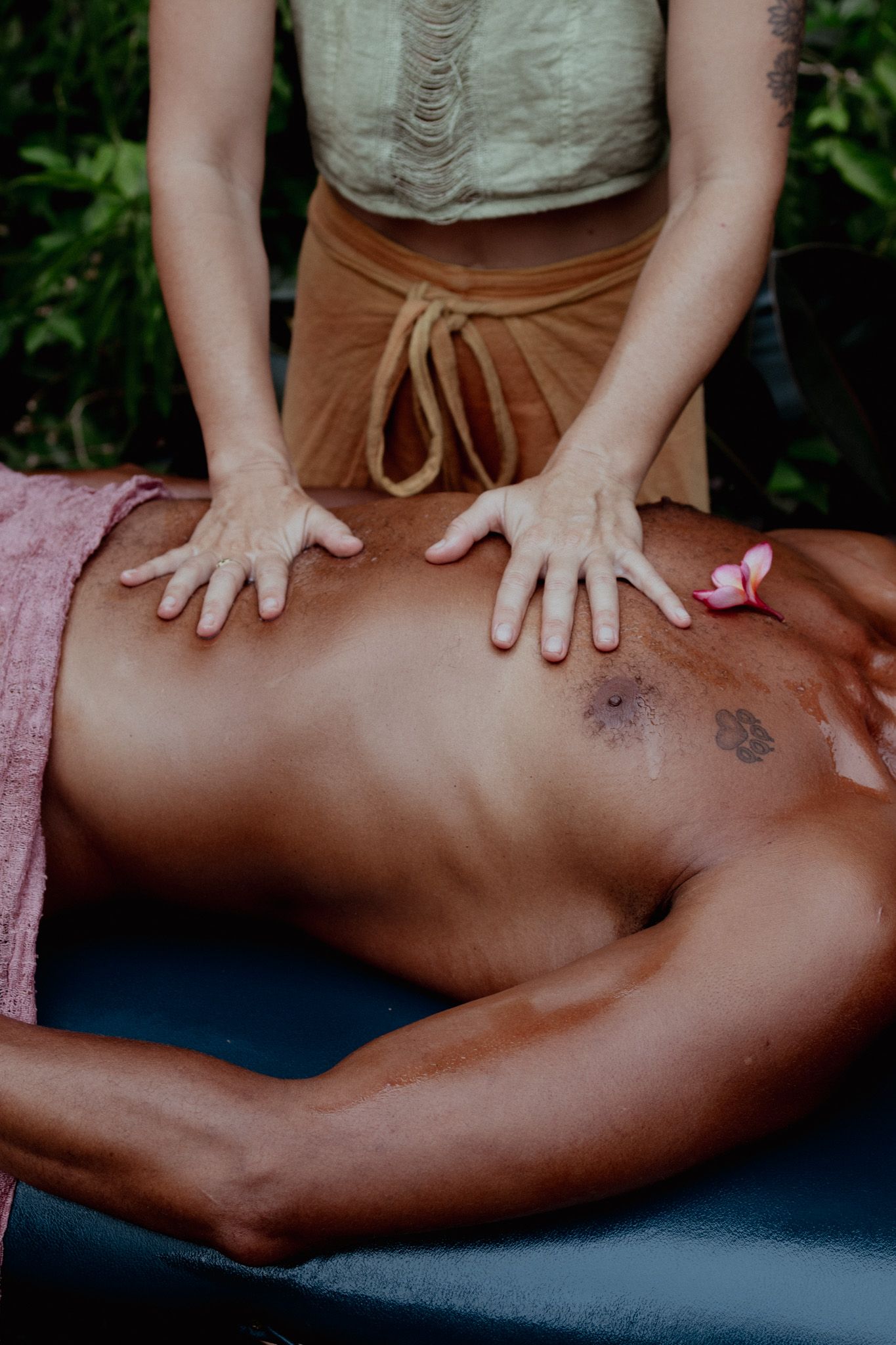 Hands perform deep tissue massage techniques on a client's back during an outdoor spa treatment.