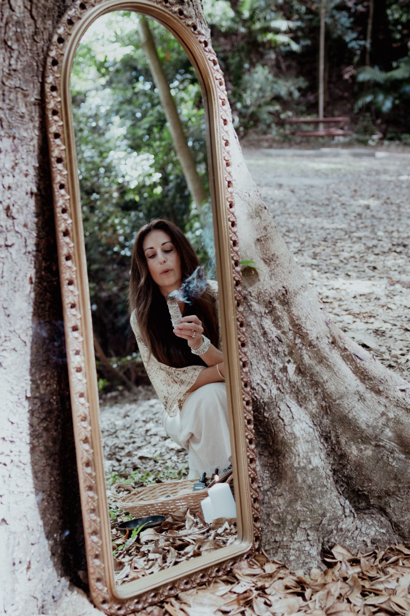 Vintage mirror leans against tree trunk reflecting a dreamy forest portrait.