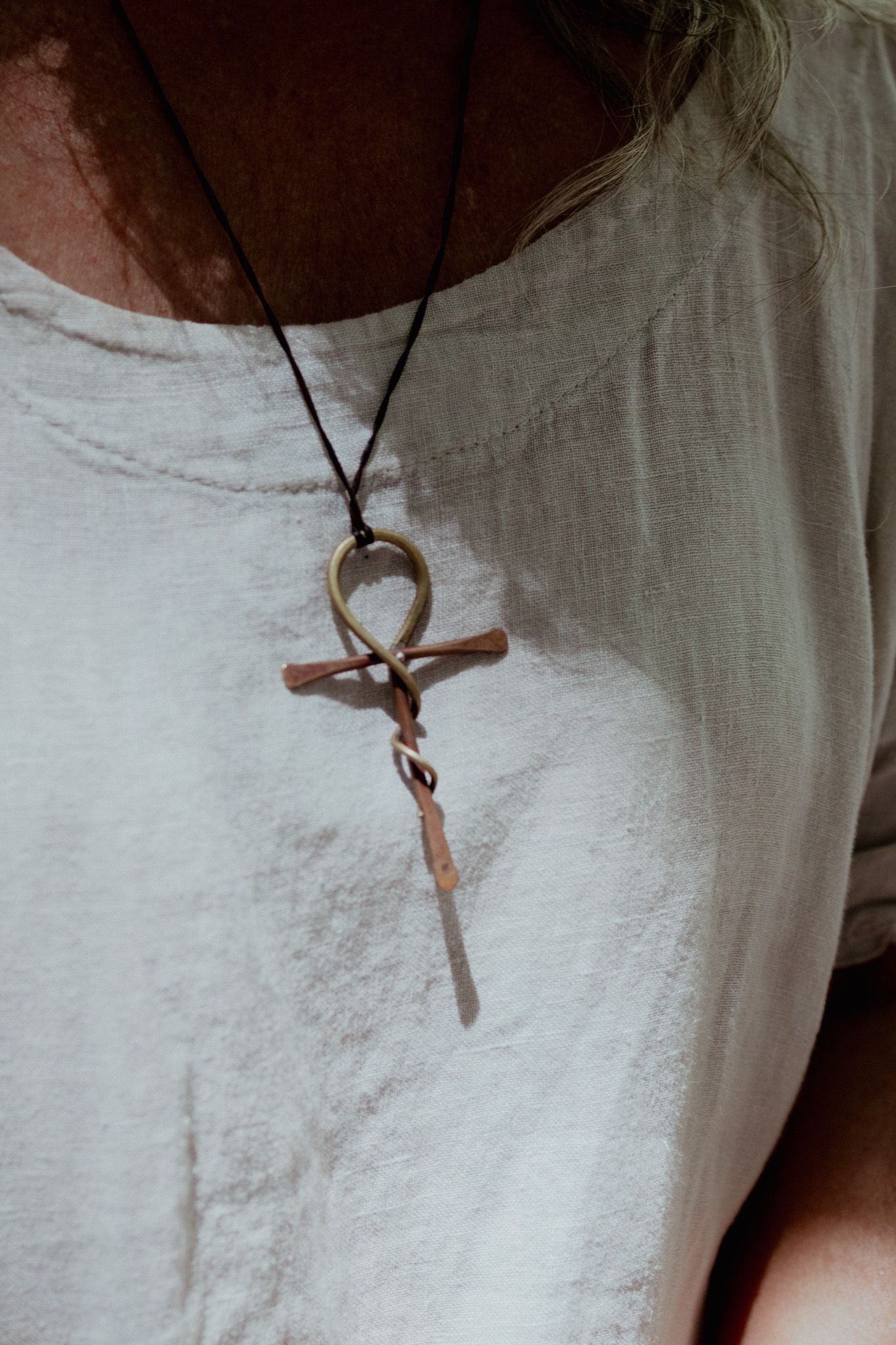 Detail shots of a pendant necklace against white linen clothing.