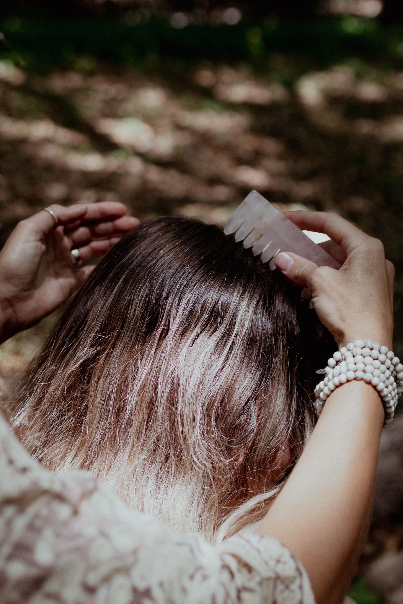 Hands styling hair with a comb in a forest setting.