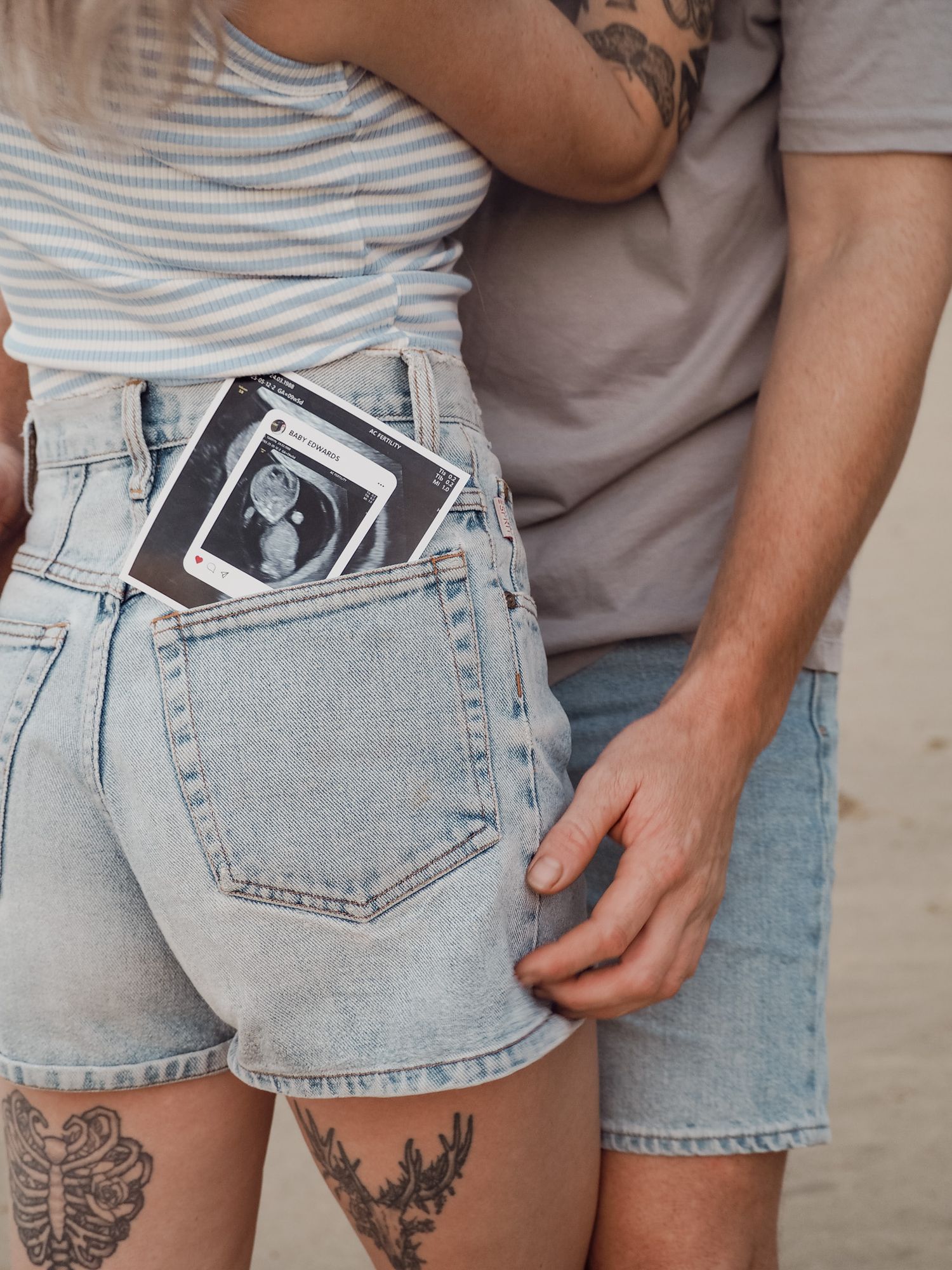 Ultrasound photos tucked into back pockets of denim shorts with leg tattoos visible.