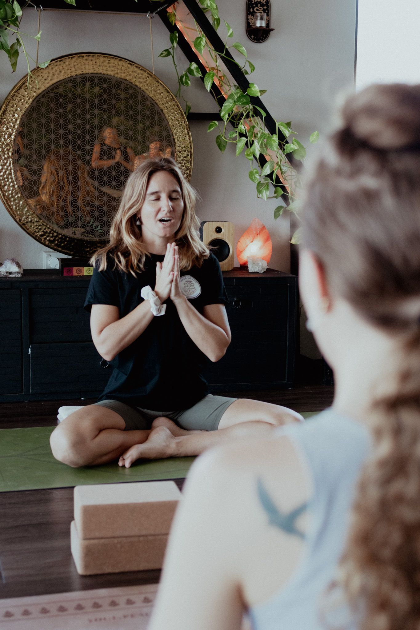 Indoor yoga session with instructor demonstrating poses on a mat with decorative elements in background.