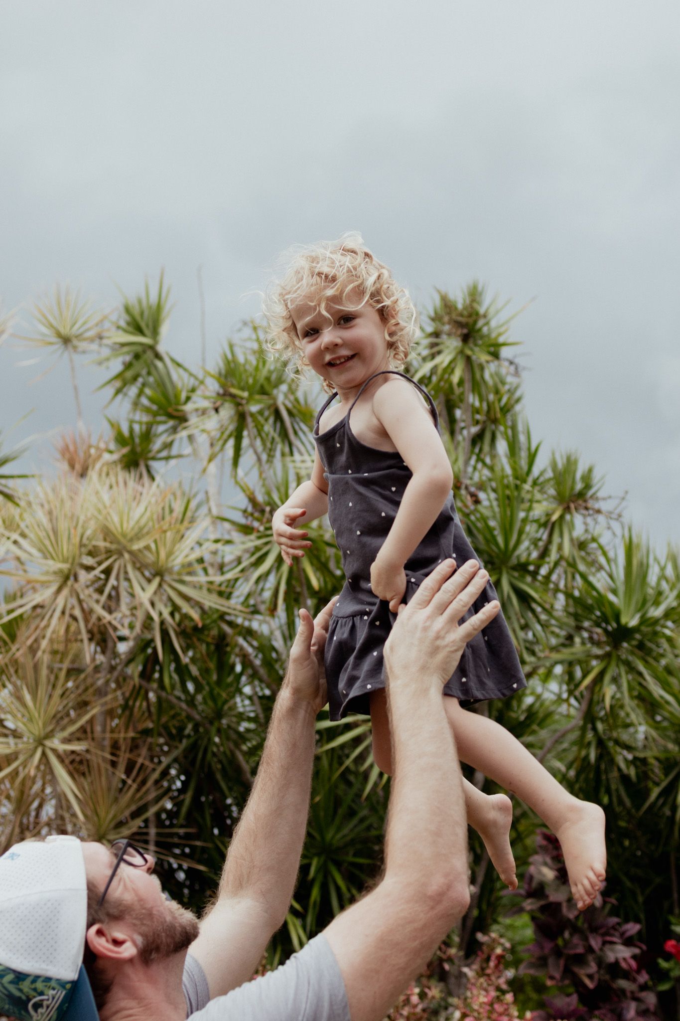 Joyful moment of a child being lifted high in the air with tropical plants in the background.