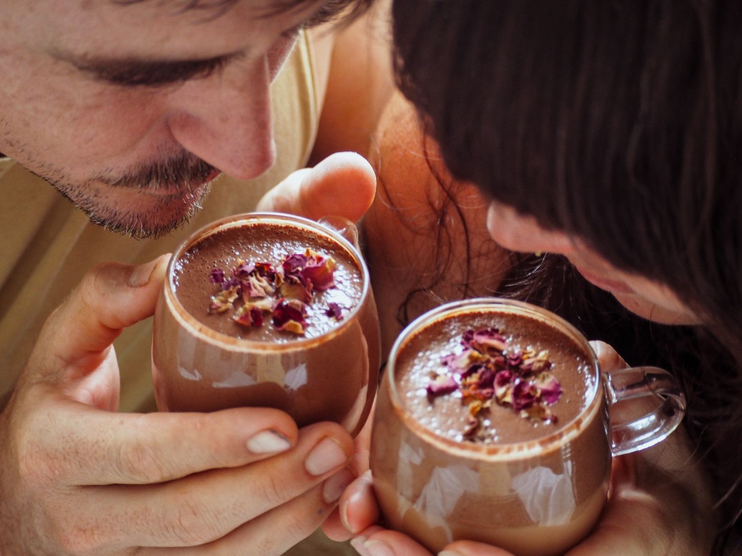 Two people sharing chocolate desserts in glass jars with spoons.