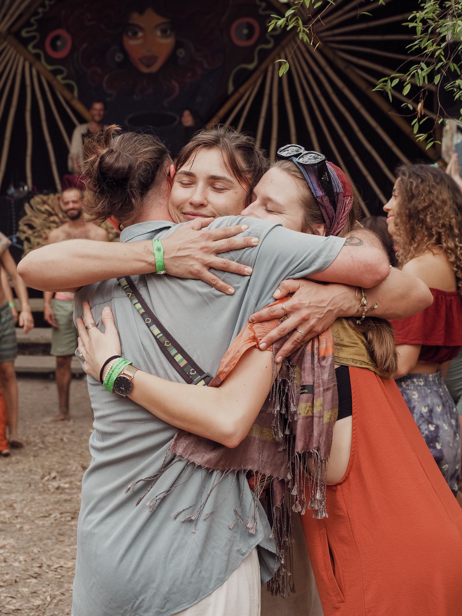 Group sharing emotional embrace at outdoor festival with decorative sunburst backdrop.
