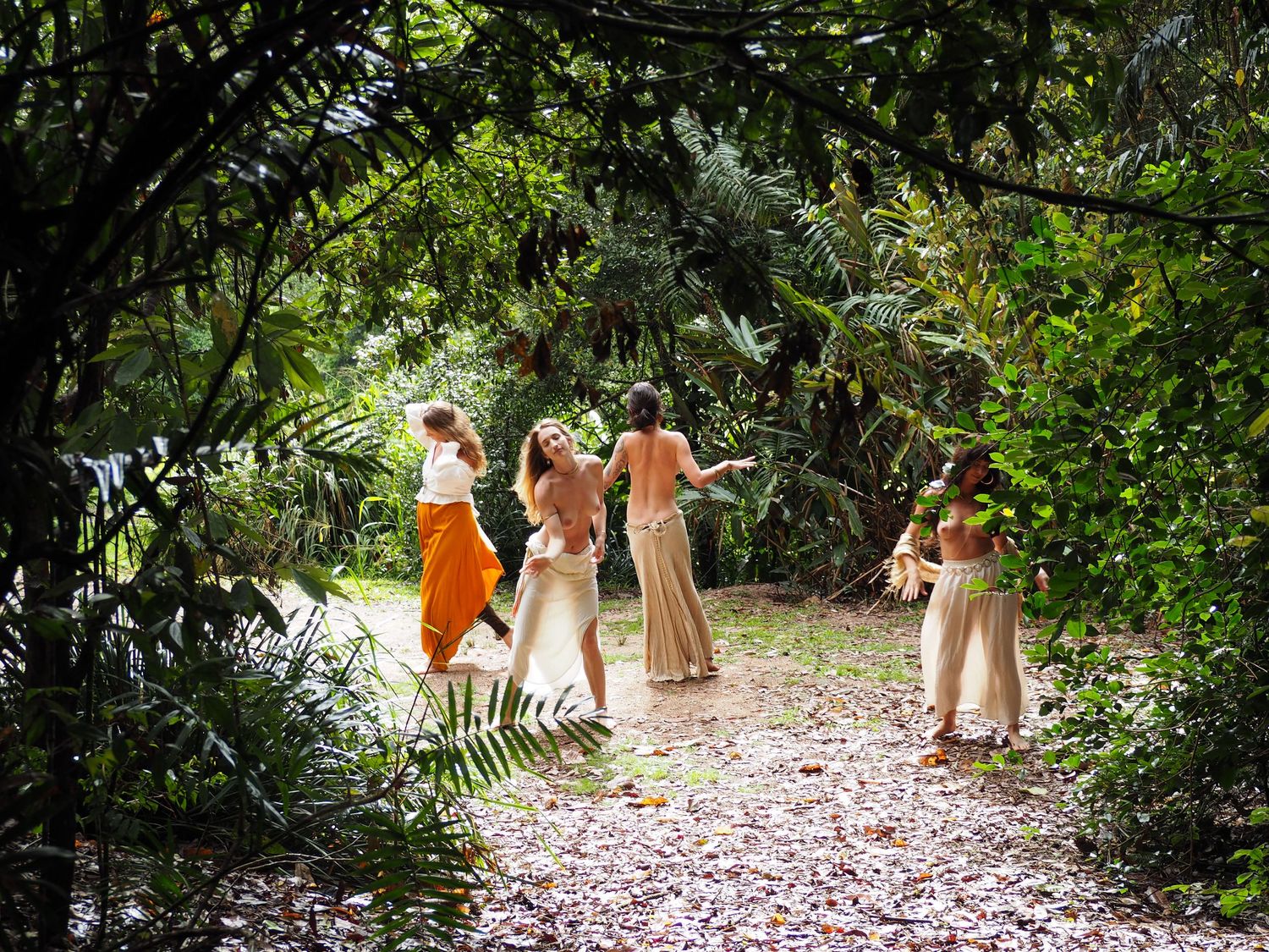 Several people in light colored dresses walk through a garden path with fallen petals.