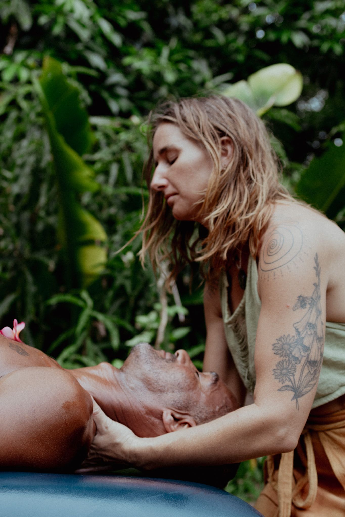A therapeutic massage session takes place on a table surrounded by lush greenery.