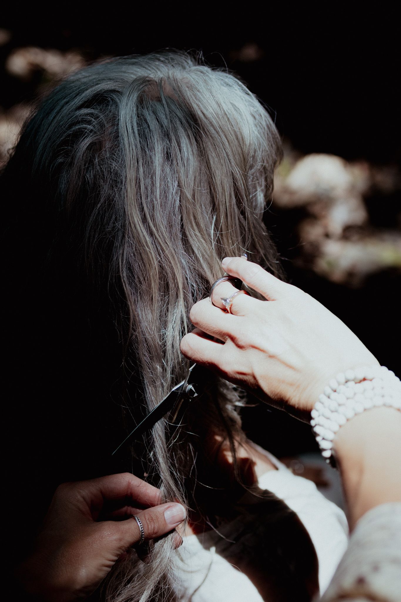 Hands styling silver-gray hair with jewelry details visible.