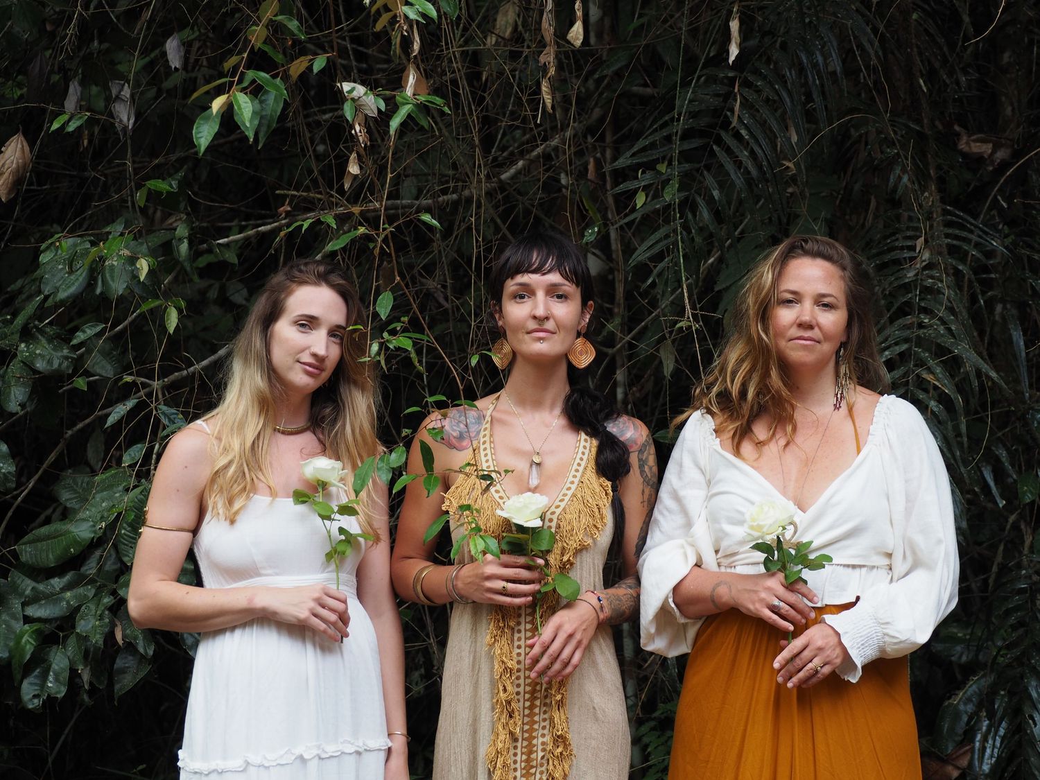 A group poses together in white and mustard colored dresses holding flowers.