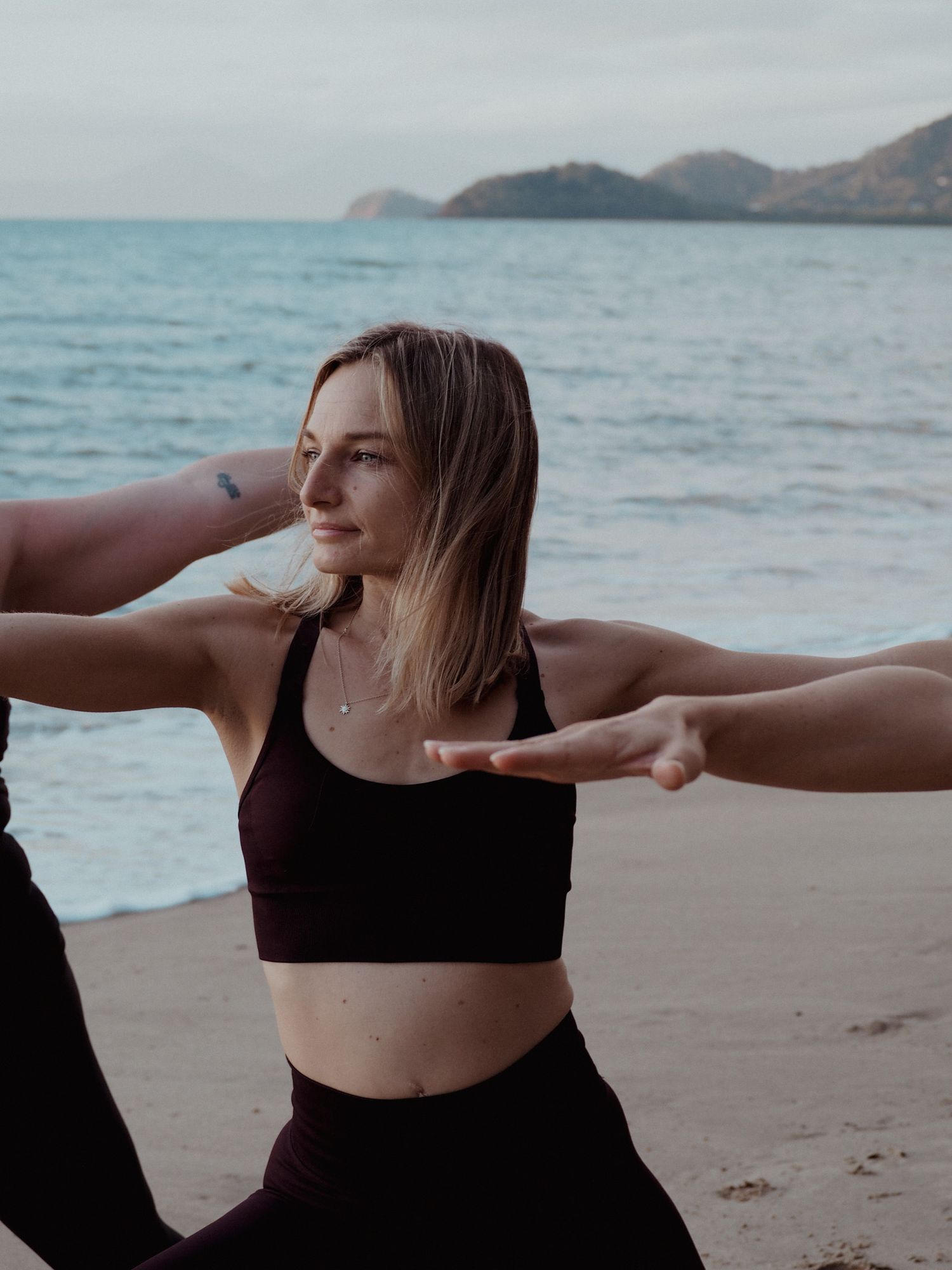 A group practices dance or yoga movements on a beach at dusk.