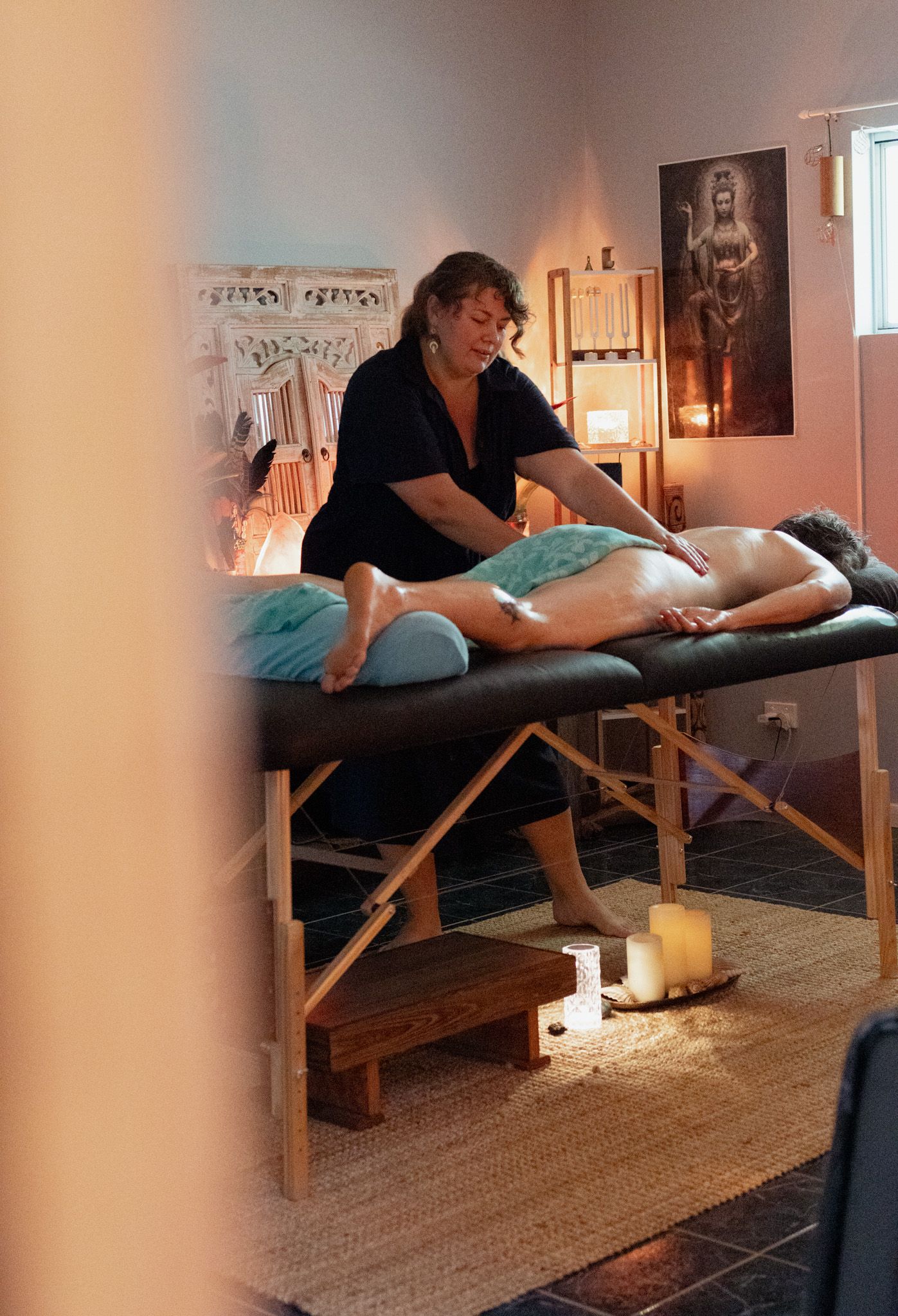 Massage therapist works on a client lying face down on a massage table in a candlelit spa room with warm, calming decor.