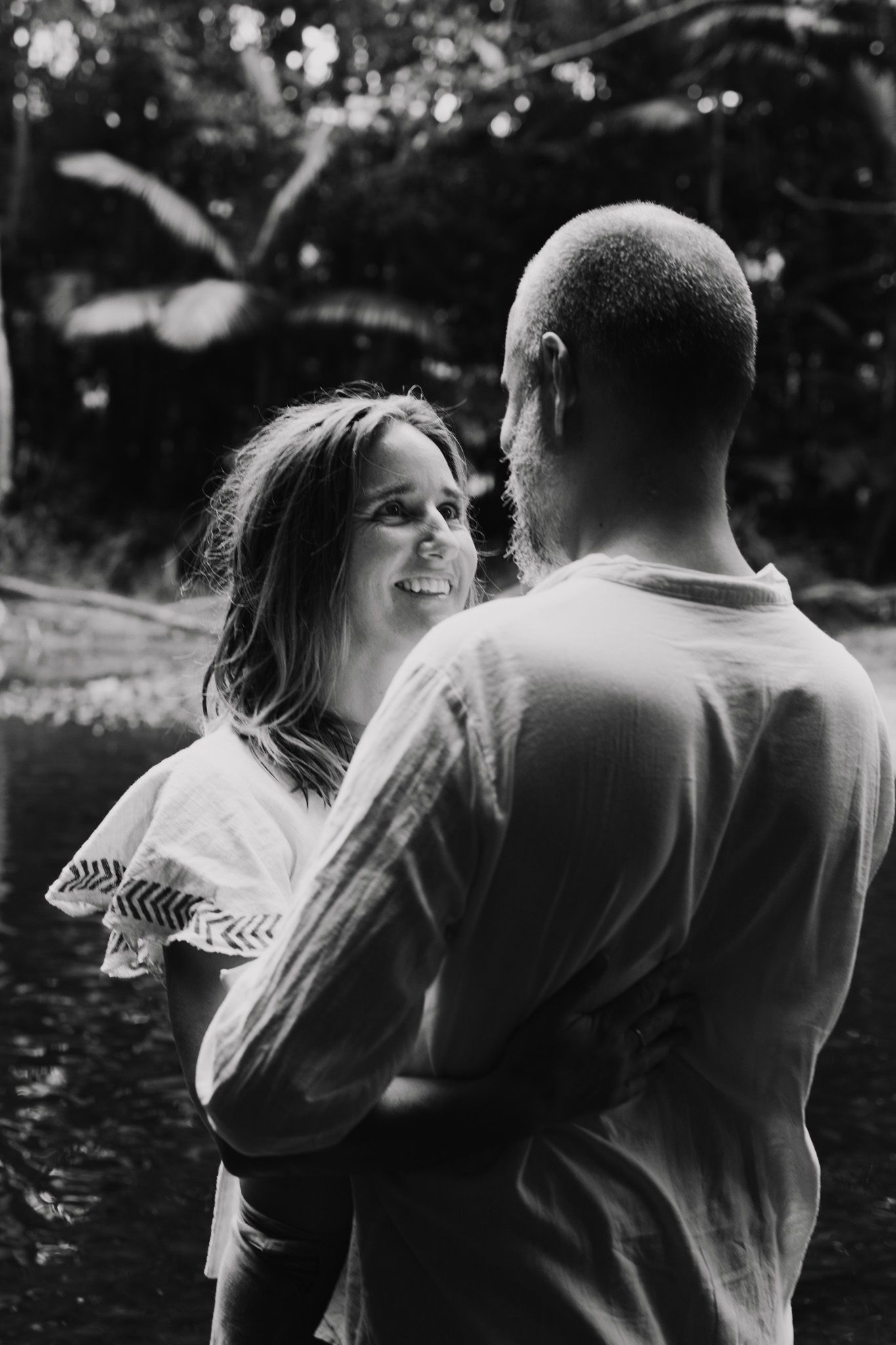 Couple embracing and laughing together outdoors in black and white photography.