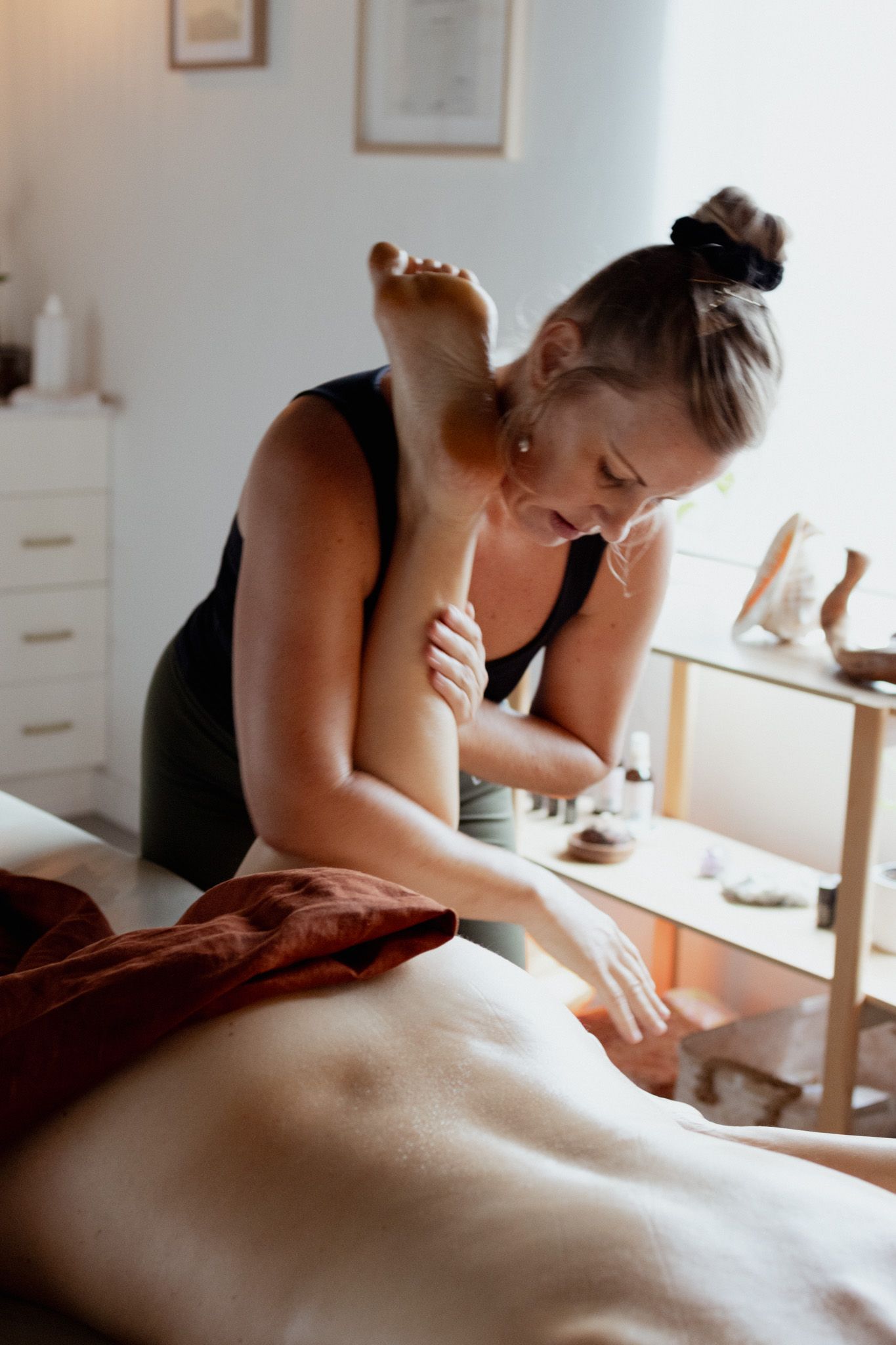 Massage therapist in black tank top performs therapeutic treatment in bright spa room.