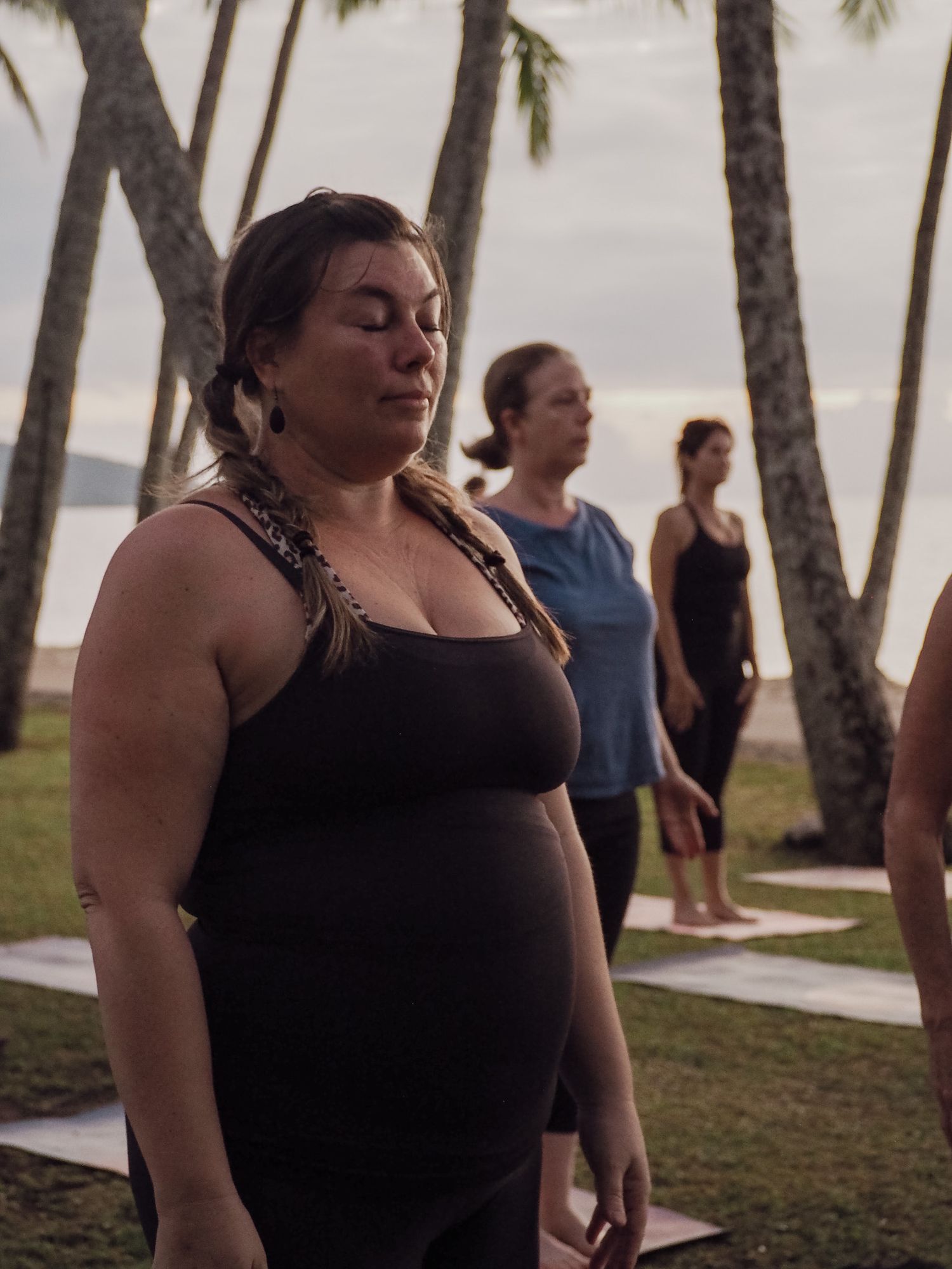 Person in black tank top practicing mindful breathing during outdoor yoga session near palm trees.