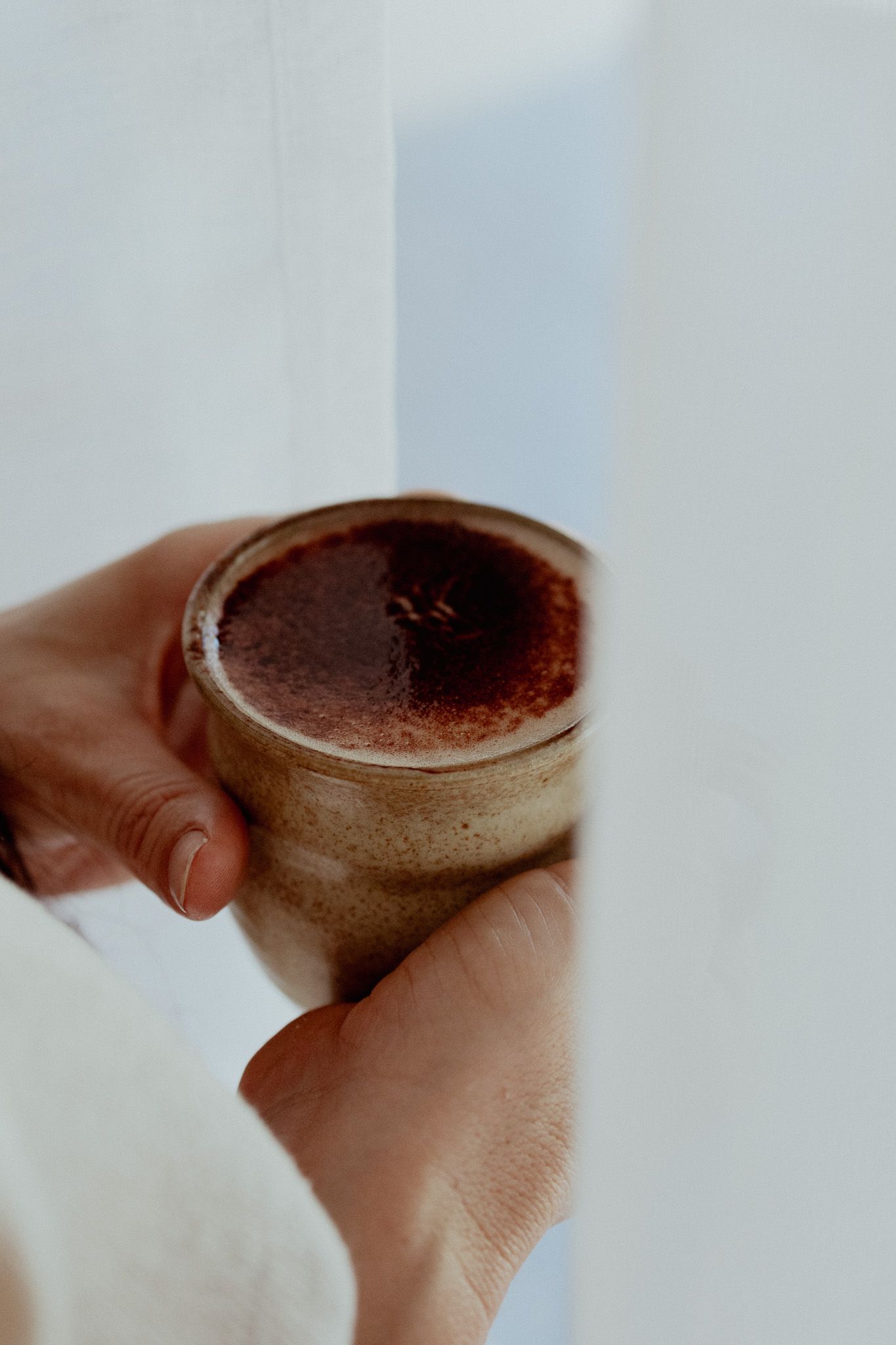 Close-up shot of hands holding a ceramic cup with dark liquid.
