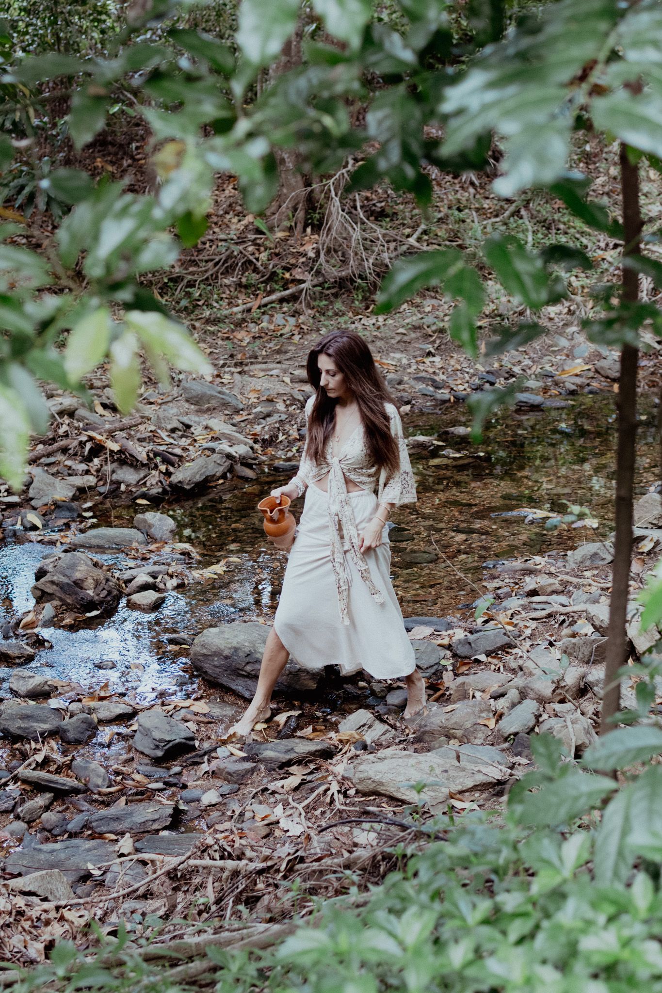 A dreamy forest photoshoot with someone sitting among rocks near a stream.