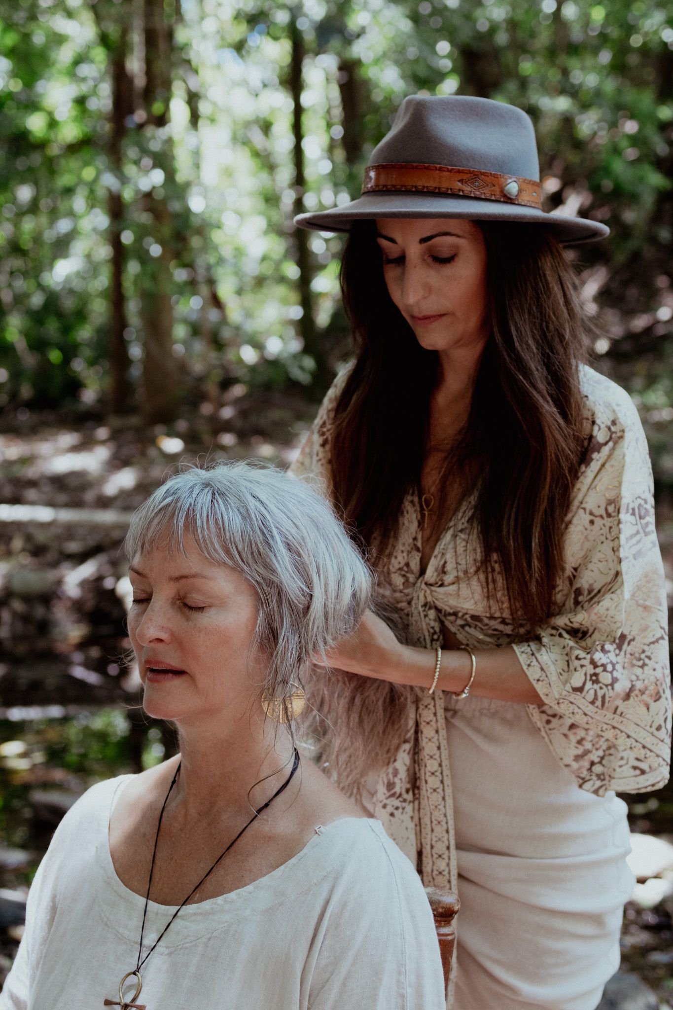 A tender interaction between two figures wearing white in a wooded outdoor setting.