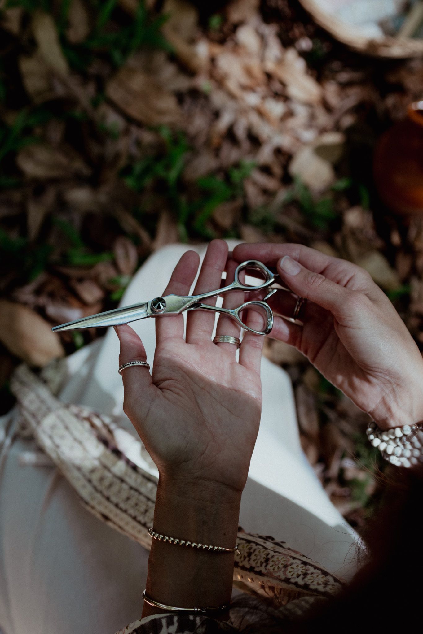 Hands holding delicate jewelry pieces against a background of dried autumn leaves.