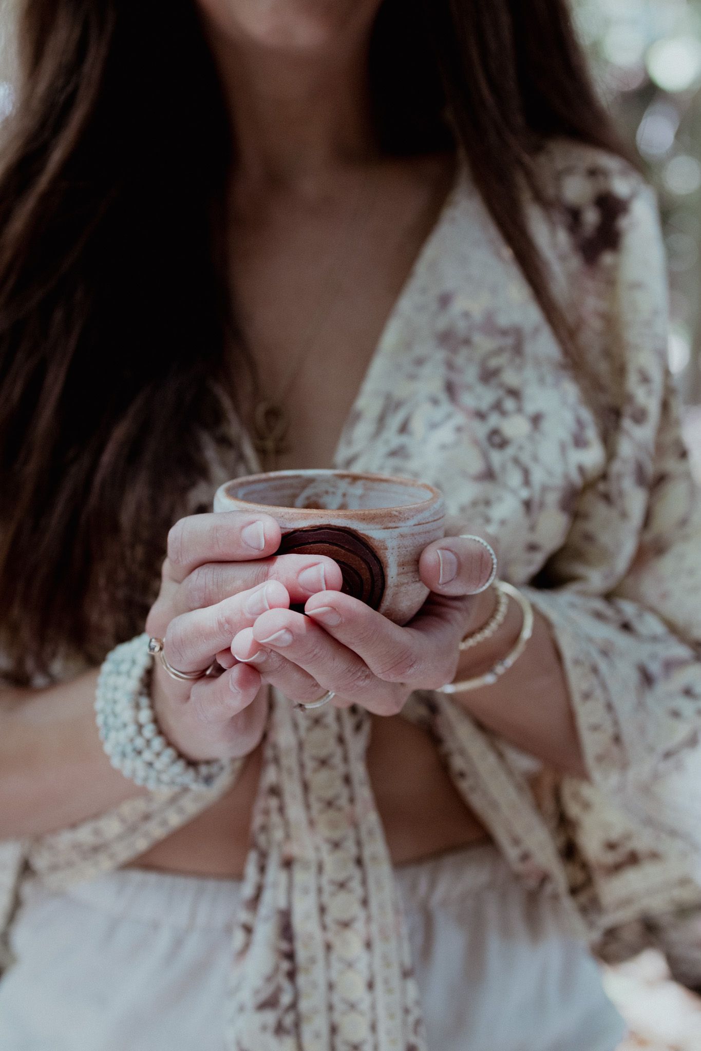 Close up of hands holding delicate teacup with lace and pearl details.
