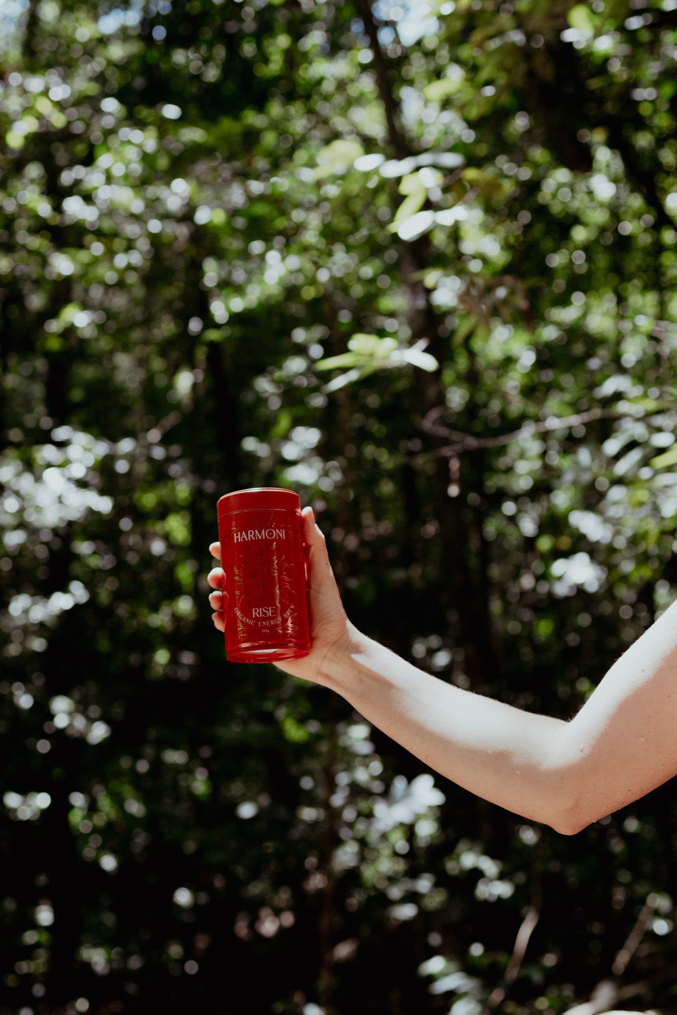Hands holding a red glass bottle against sunlit green foliage background.