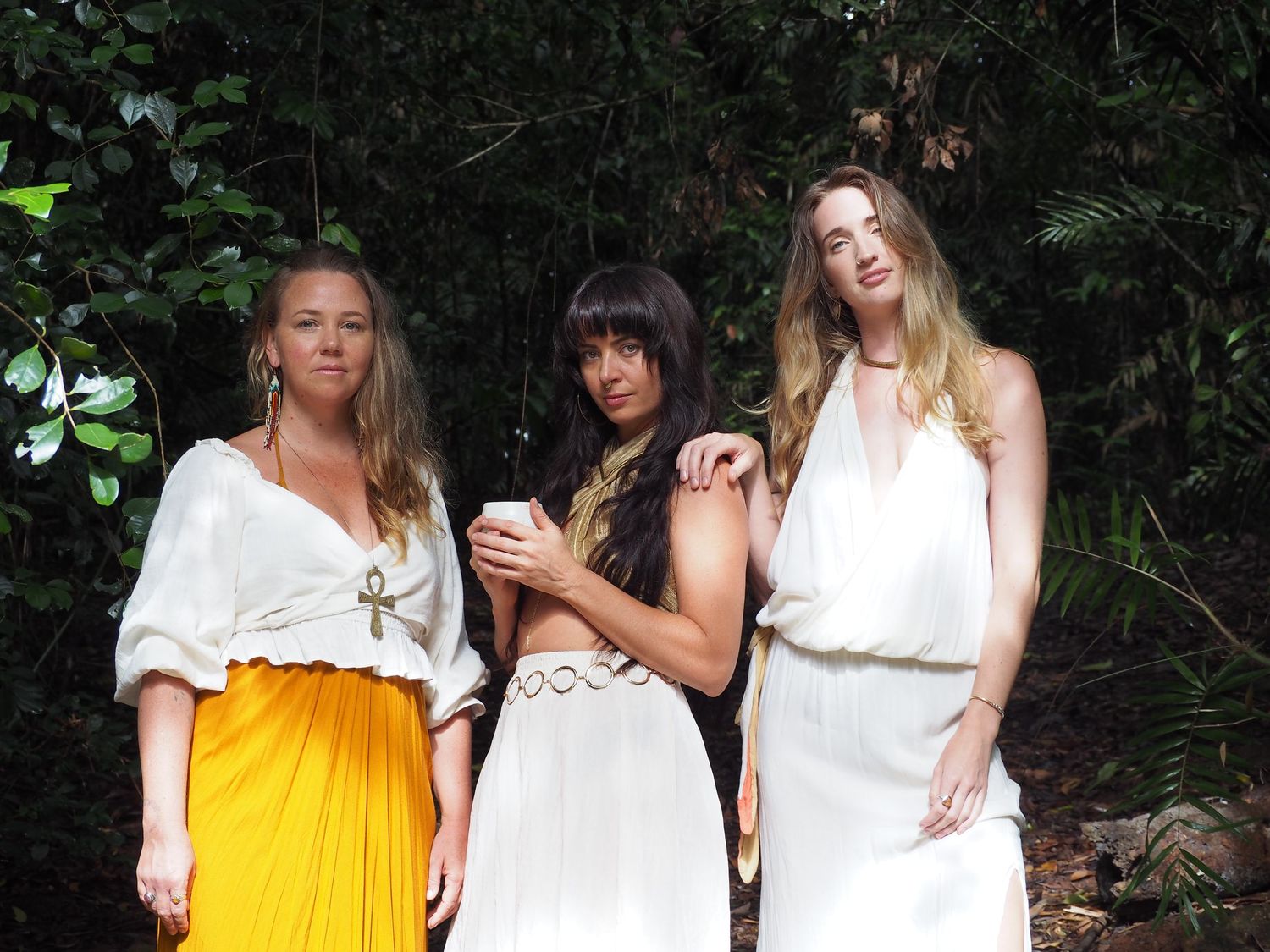 Group wearing white and yellow dresses pose together in tropical garden setting.