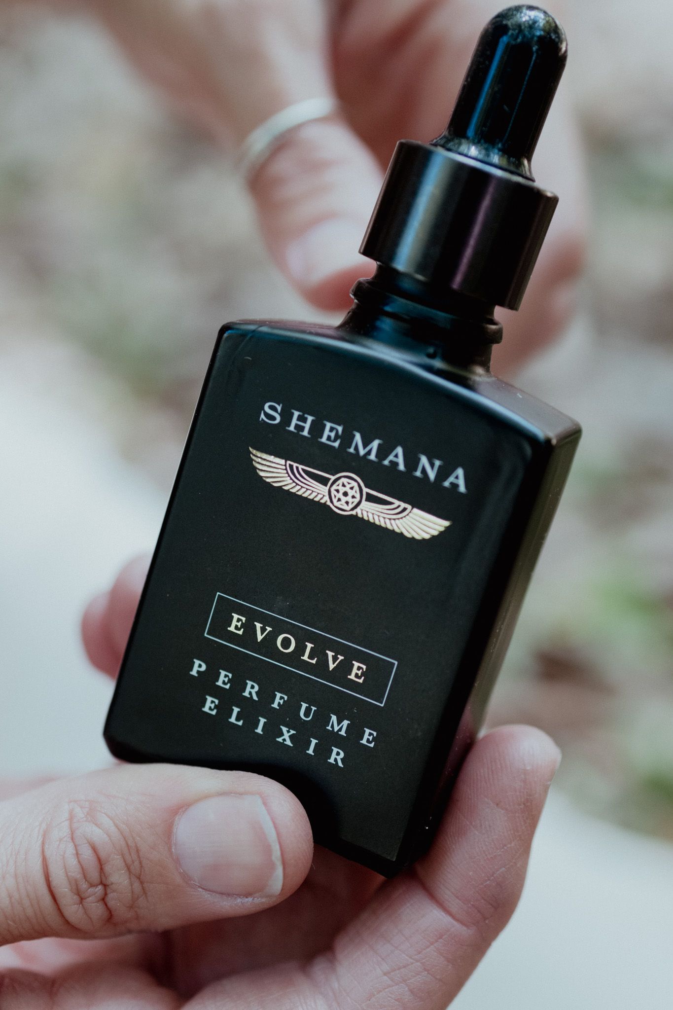 Black perfume bottle with Shemana Elixir Evolve branding held in hand.