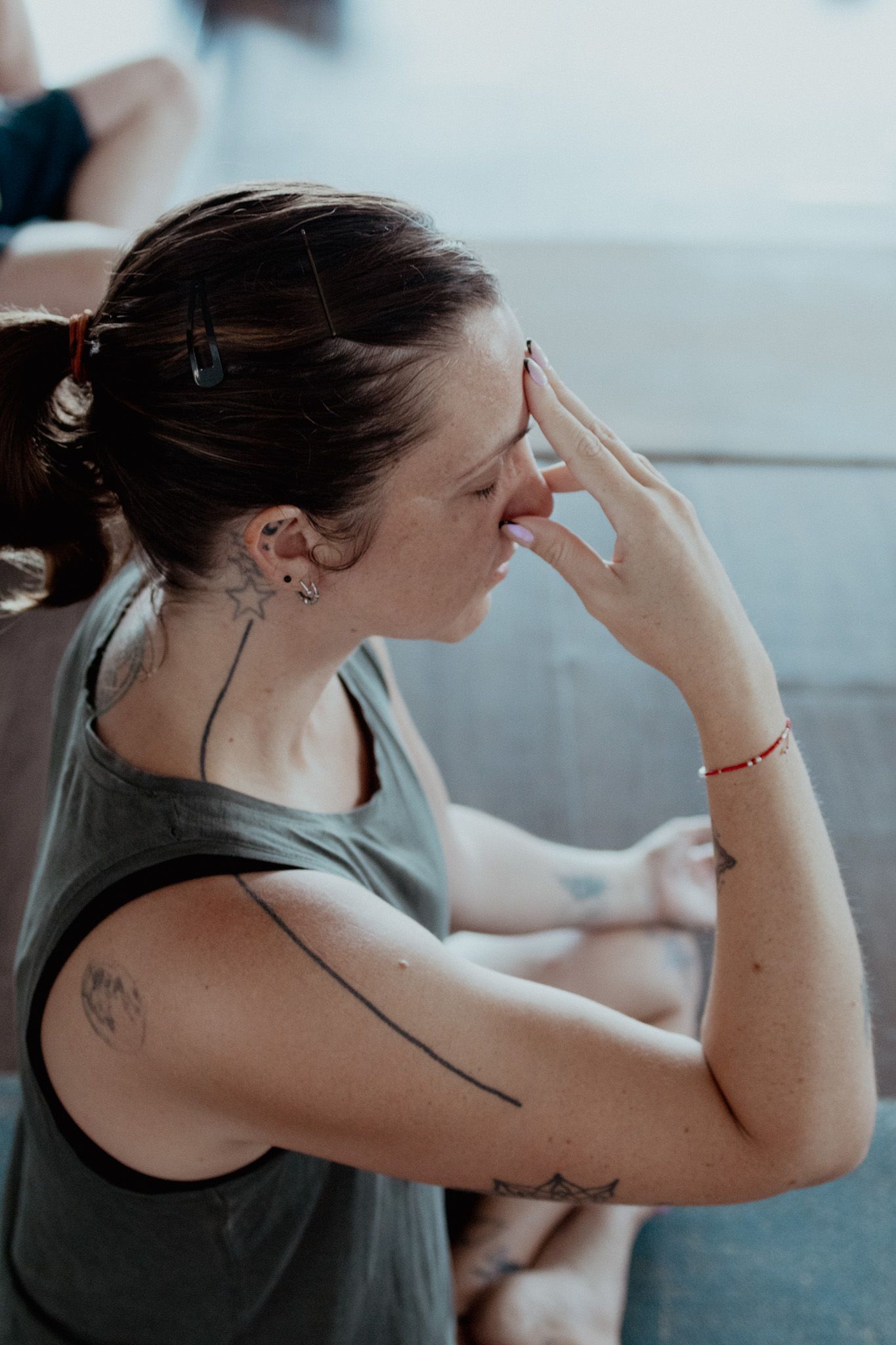 Side profile of person in gray tank top touching face with visible tattoos.