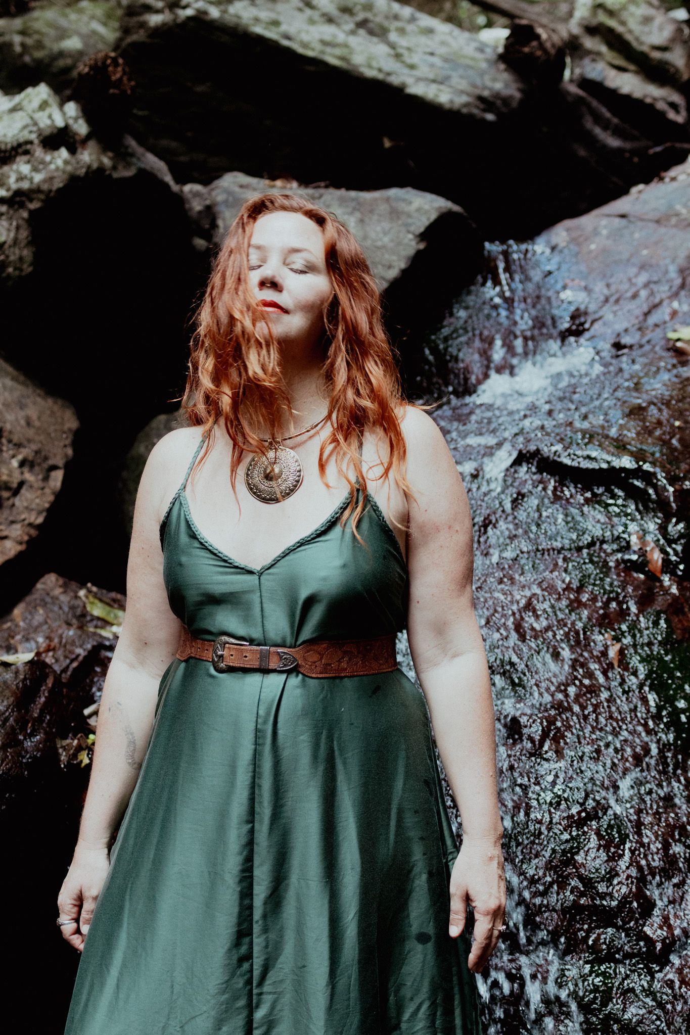 Person in green dress poses against rocky backdrop in moody outdoor photoshoot.