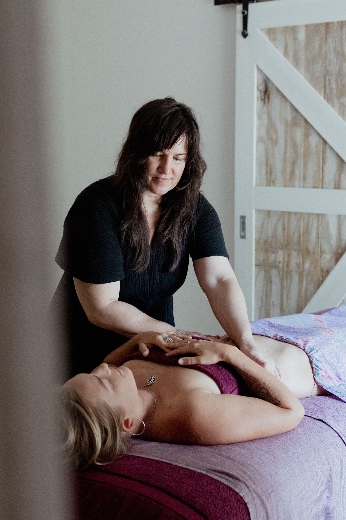 Massage therapist performs therapeutic massage techniques on client lying on purple table.