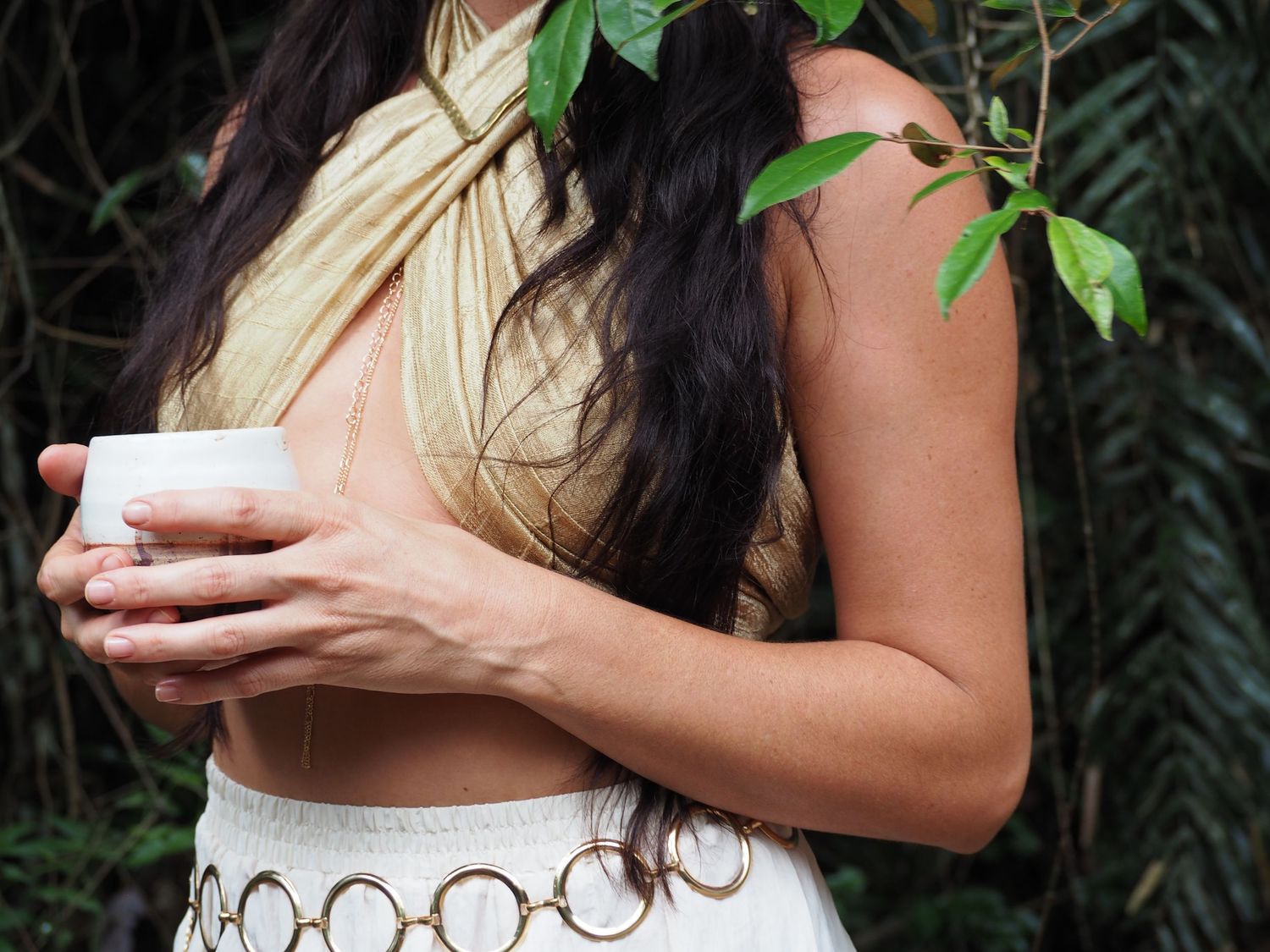 Hands holding cups against backdrop of tropical greenery.