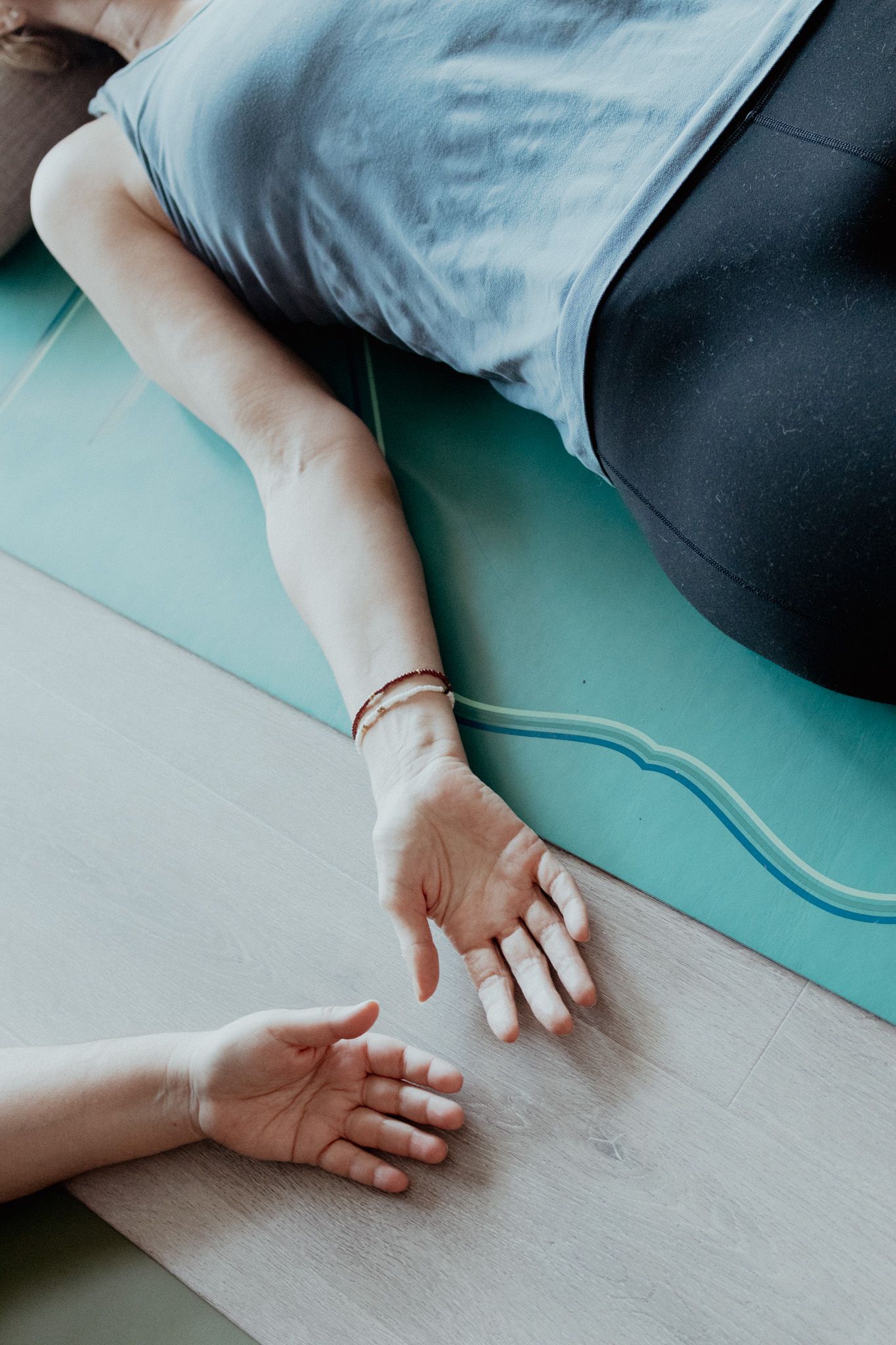 Hands resting on a turquoise yoga mat during a meditation session.