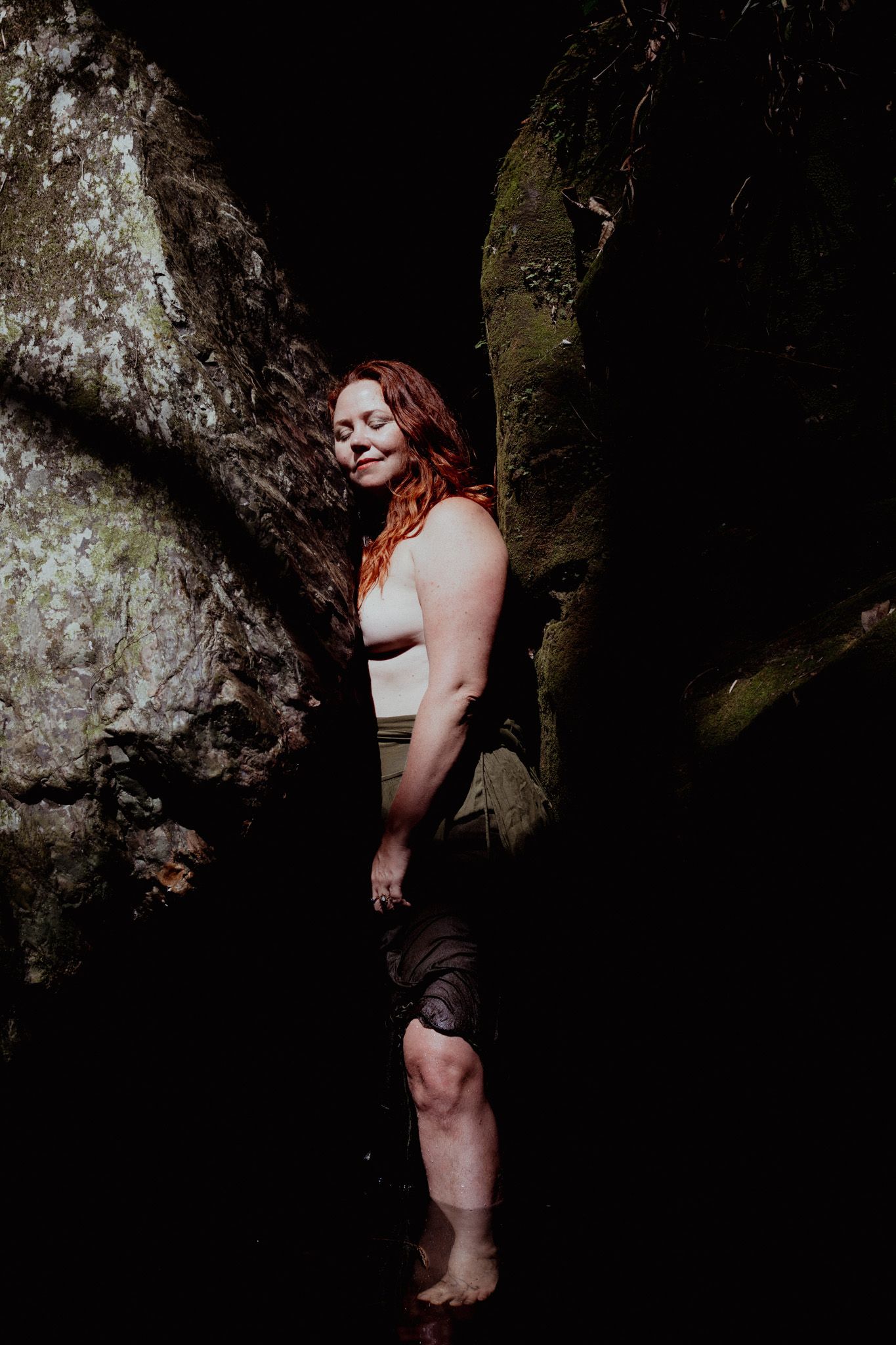 Artistic portrait against textured rock formations in dark atmospheric lighting.