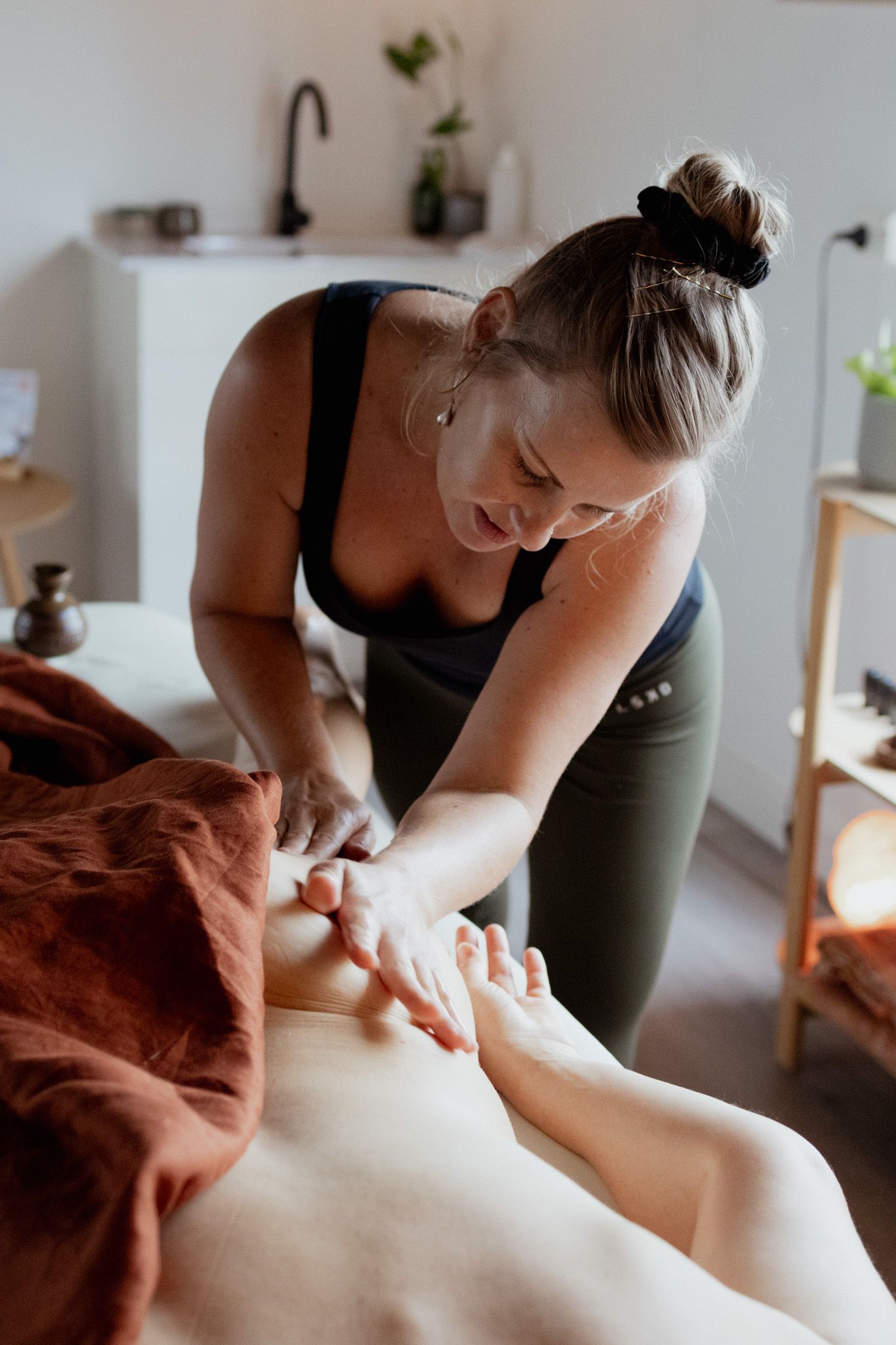 Massage therapist in athletic wear performs hand massage treatment in spa setting.