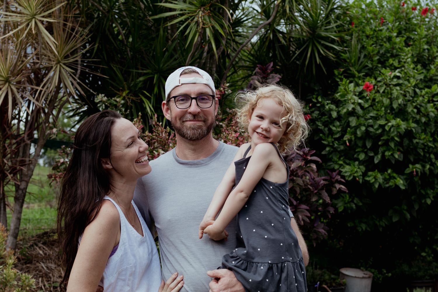Happy family moment captured outdoors with tropical plants and greenery in the background.