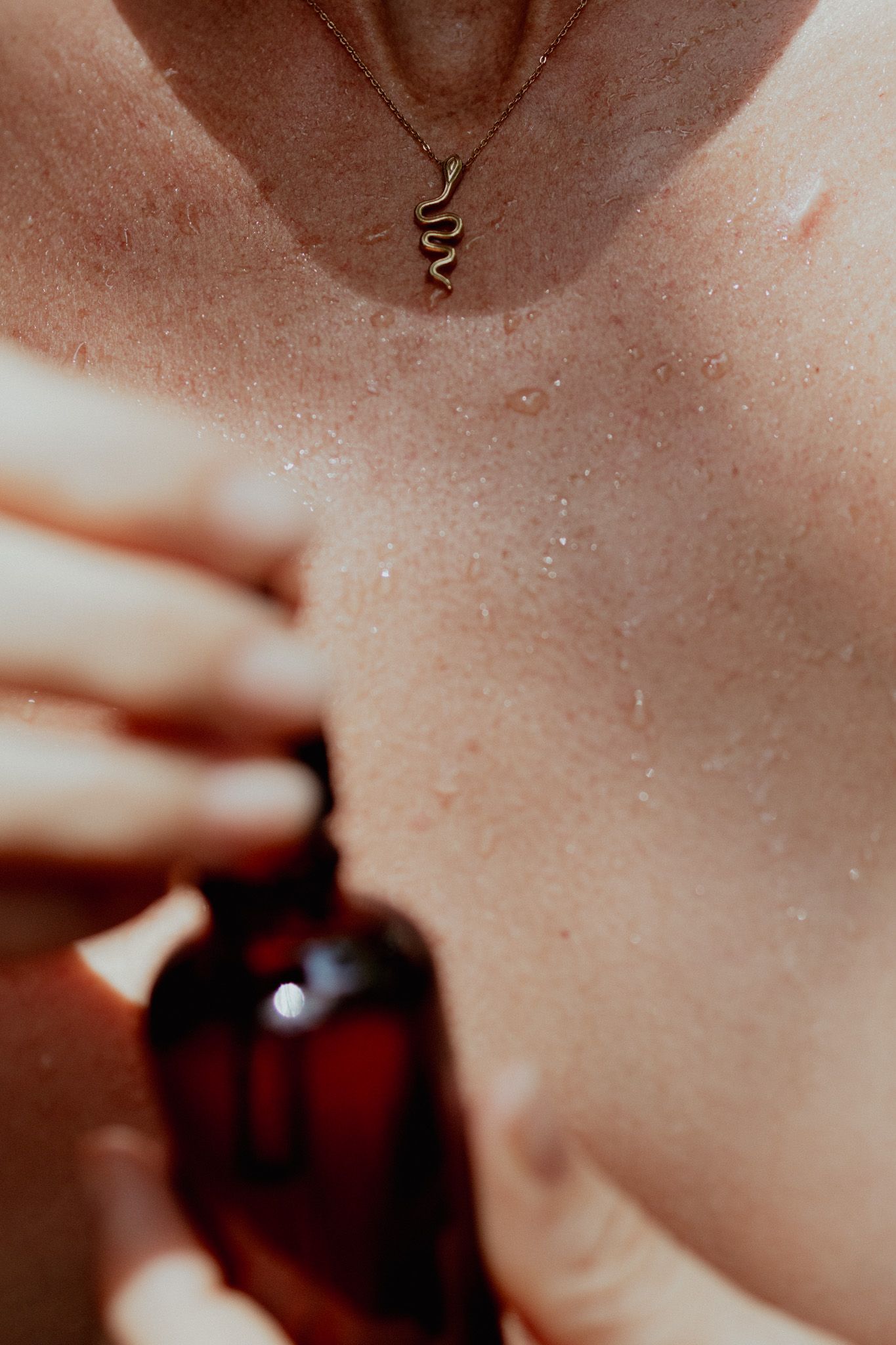 Artistic macro photography of skin and a dark glass bottle in warm tones.