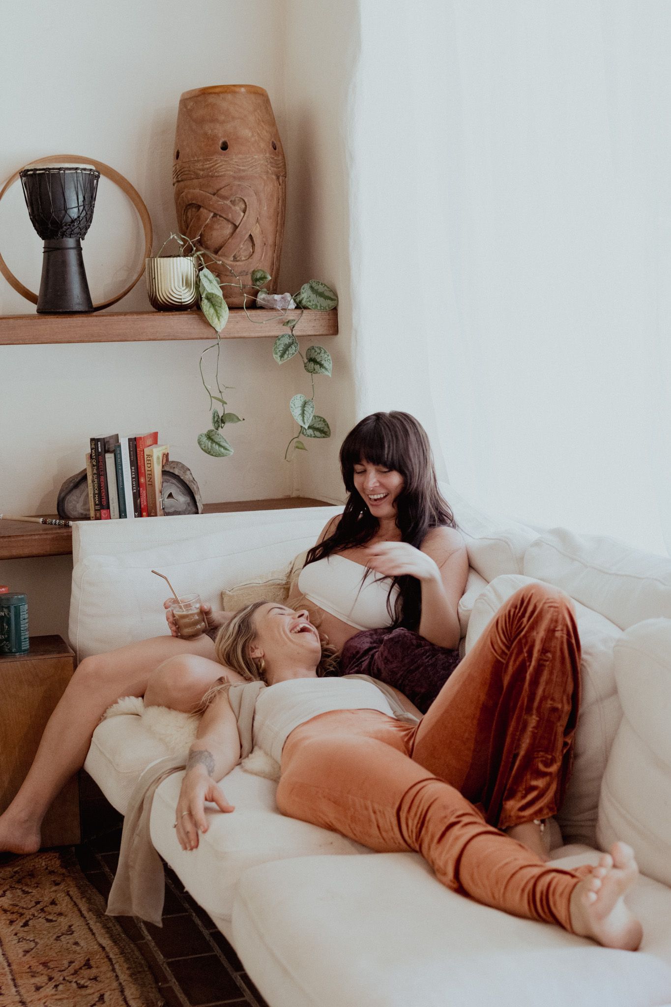 Two people lounging comfortably on a white couch with houseplants and decor visible in background.