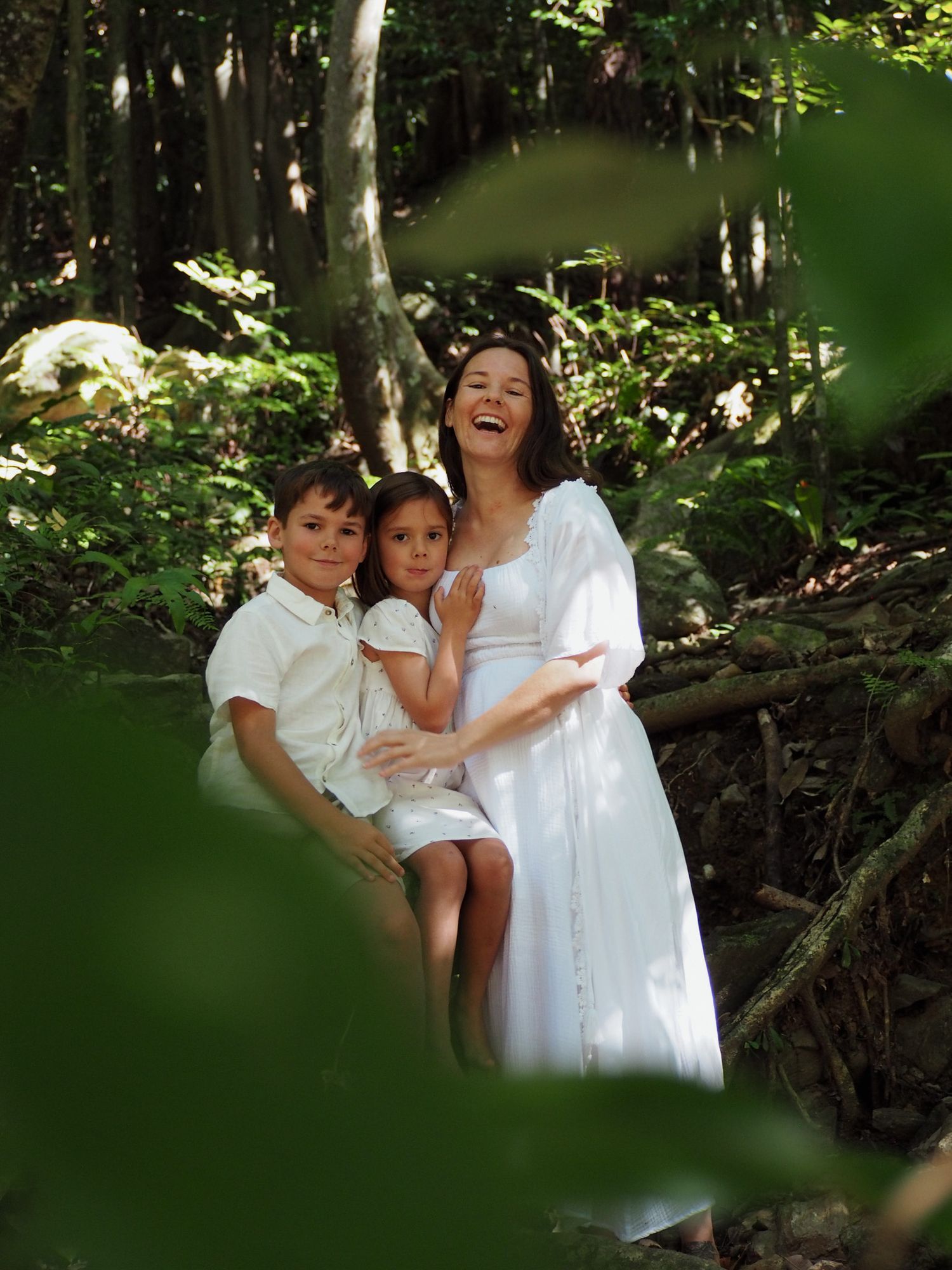 Joyful family moment captured through foliage as they pose together in a wooded setting.